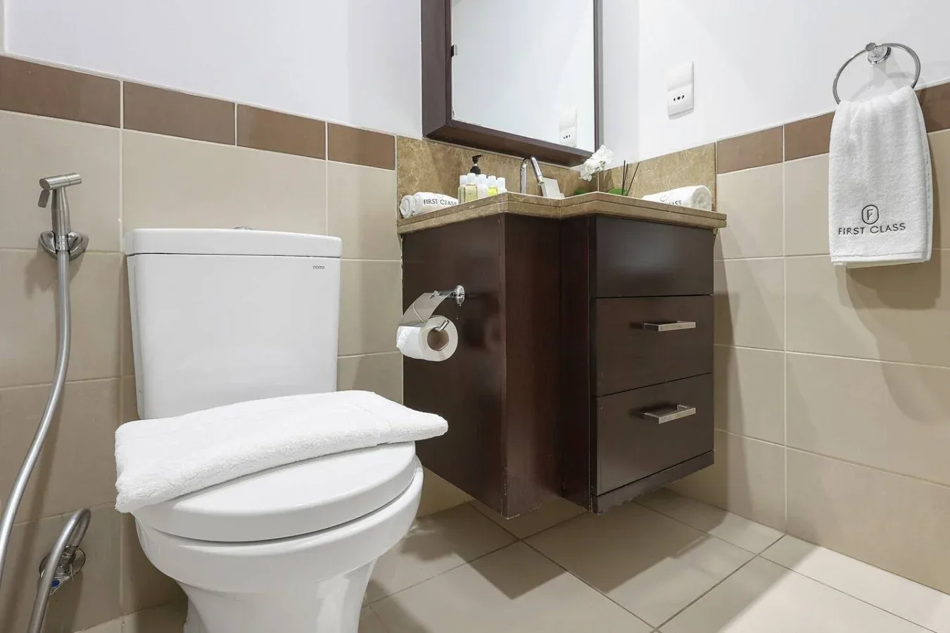 Un baño con azulejos, un inodoro, un mueble oscuro y toallas dobladas.