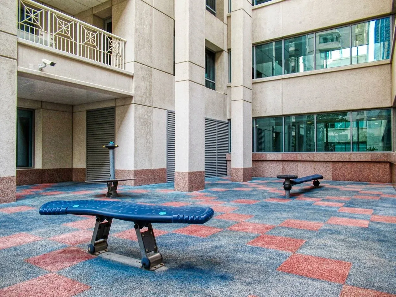 Un patio pavimentado con suelo estampado azul y rojo y varios bancos.