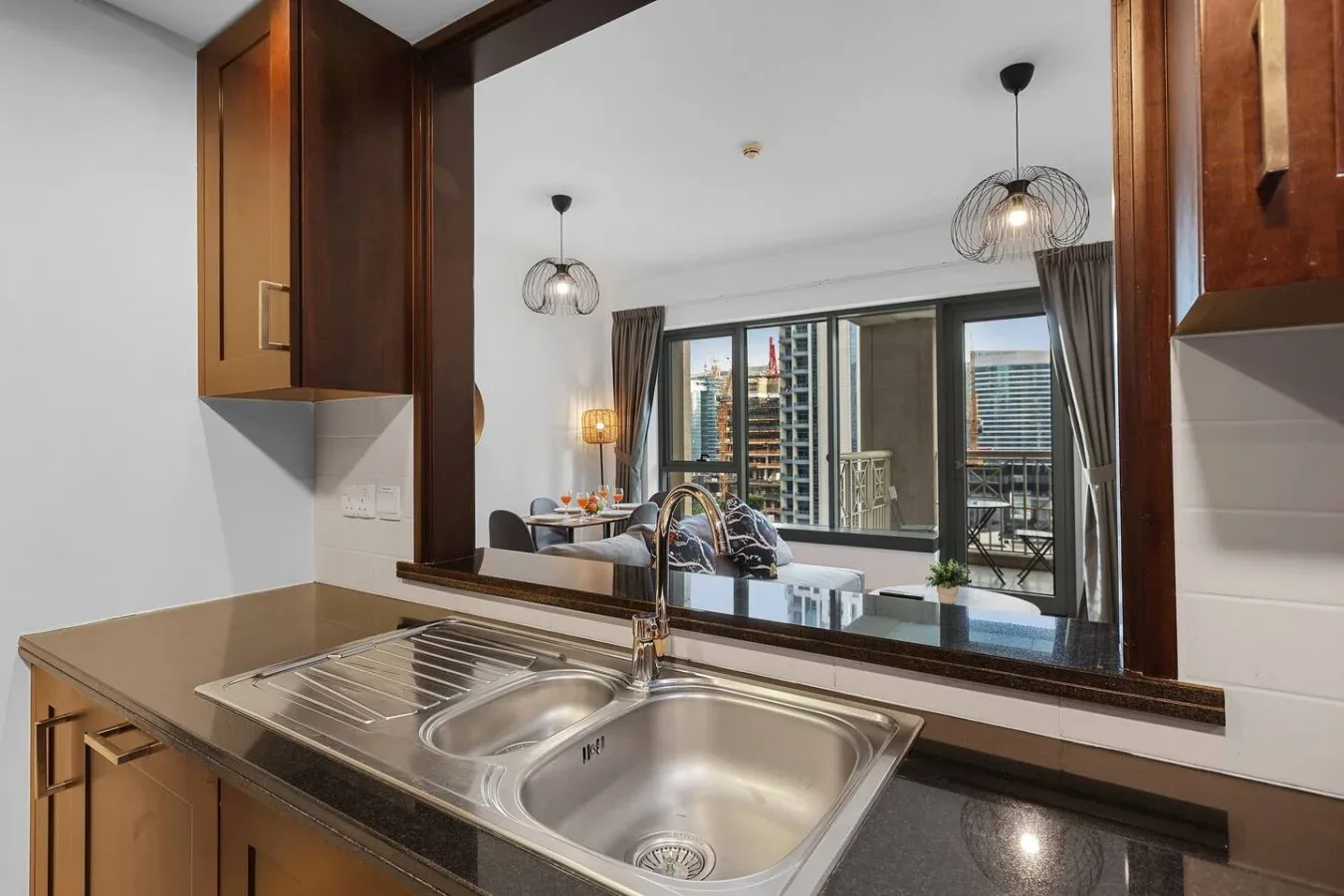 Un fregadero y una encimera de cocina dan a una gran ventana interior con edificios al fondo.
