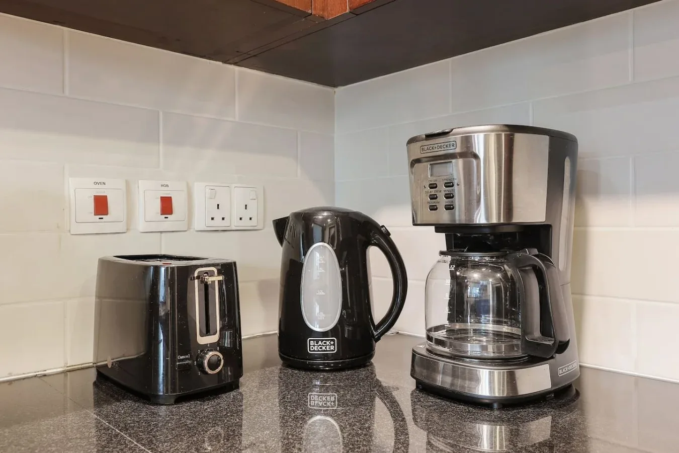 Una encimera de cocina tiene una tostadora, un hervidor eléctrico y una cafetera de goteo.