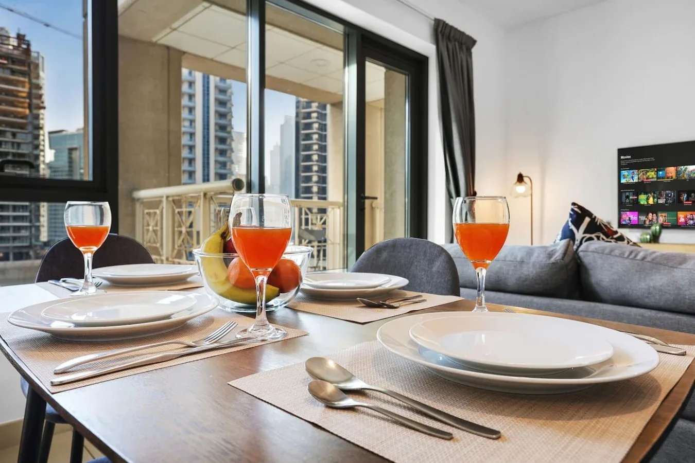 Una mesa puesta con platos y copas está junto a grandes ventanales con edificios a la vista.