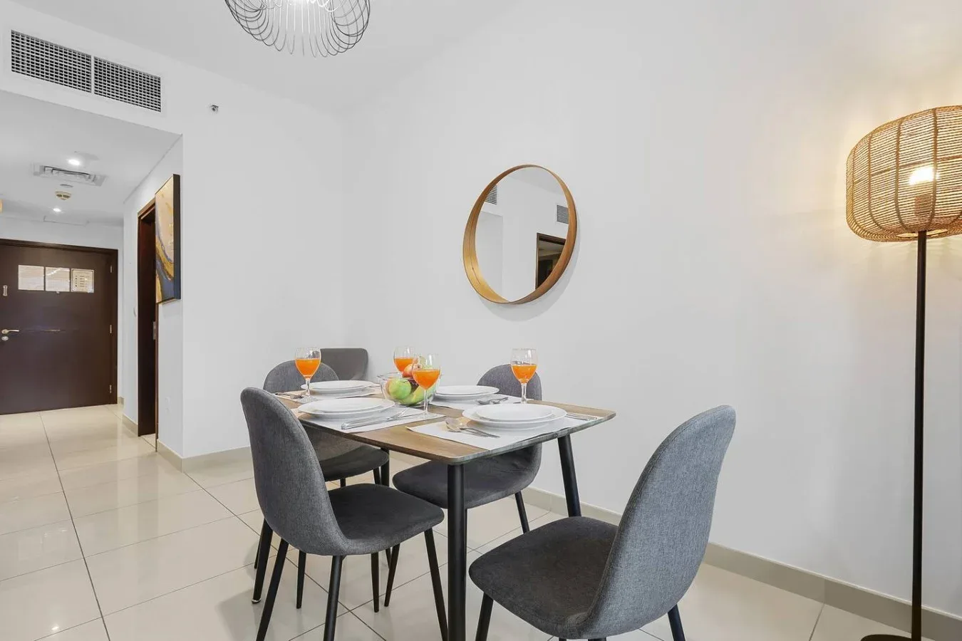 Comedor con una mesa y asientos grises bajo un espejo redondo.