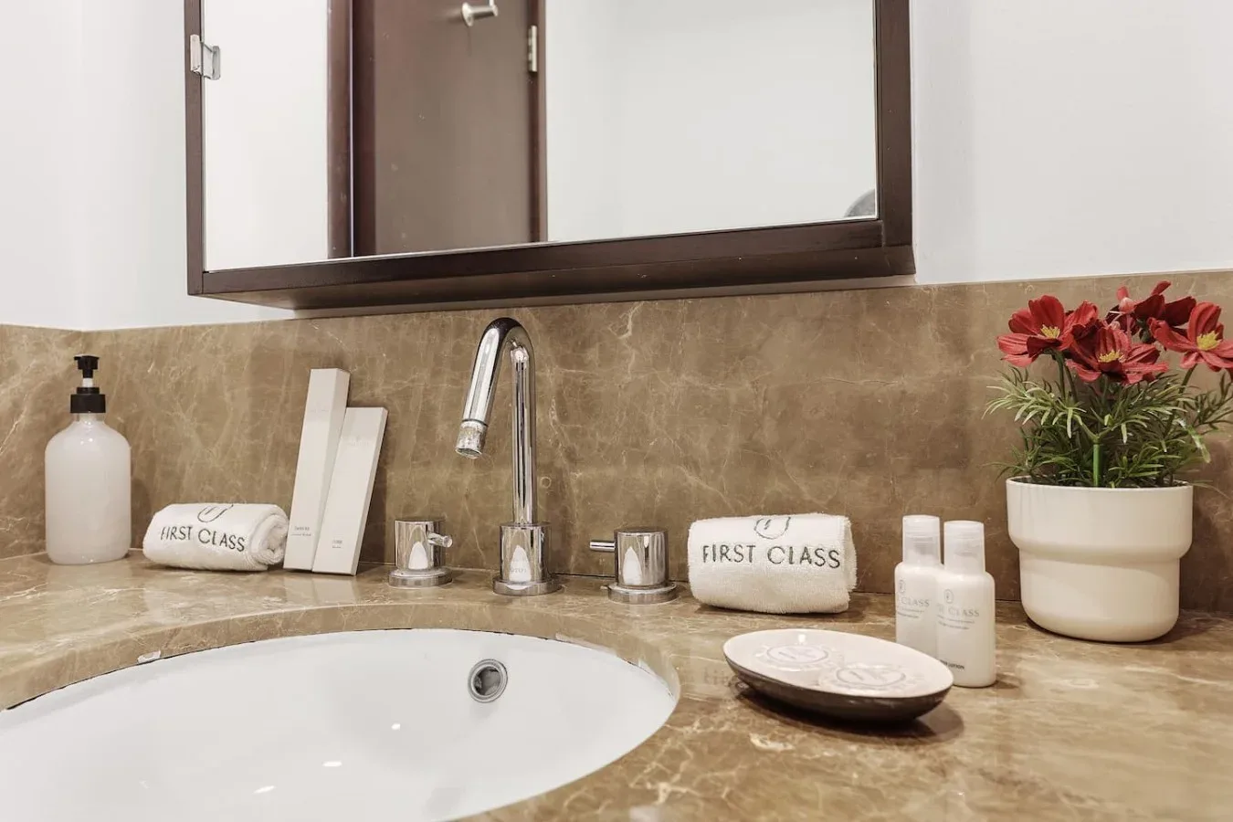 Un lavabo de baño con espejo y flores sobre la encimera.