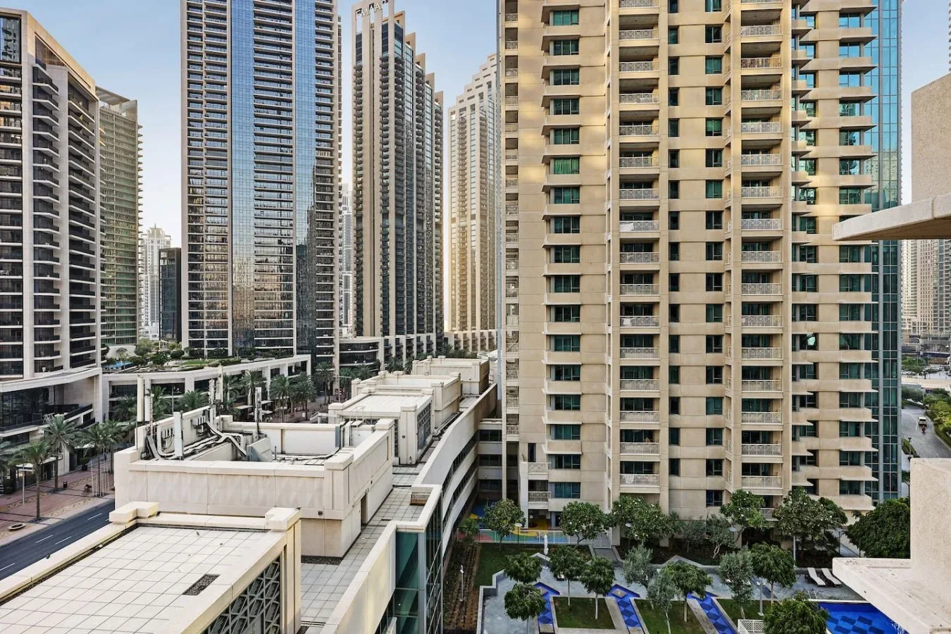 Edificios altos rodean un patio ajardinado con piscinas azules.