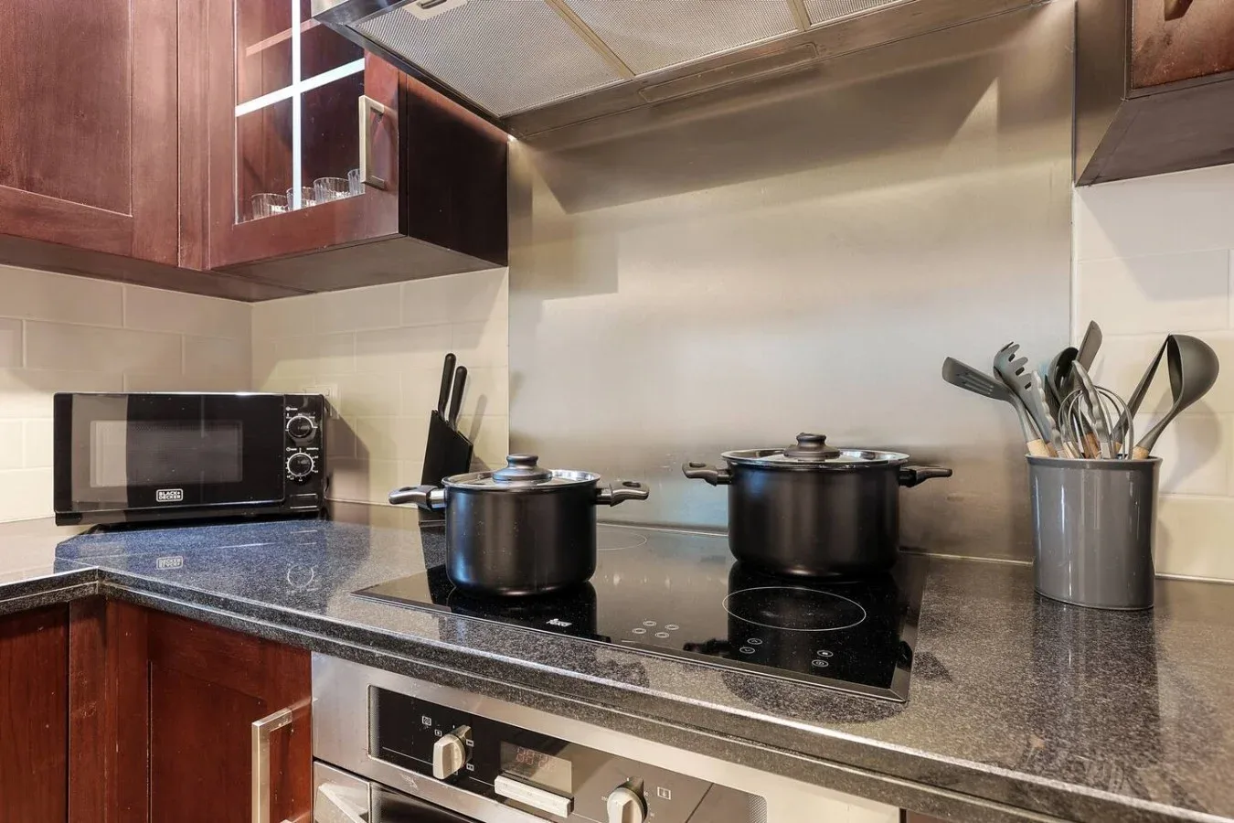 Zona de cocina con una placa, ollas y utensilios sobre la encimera.