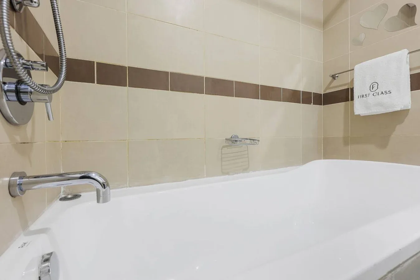 Un baño alicatado con bañera, grifo de pared y accesorios de ducha.