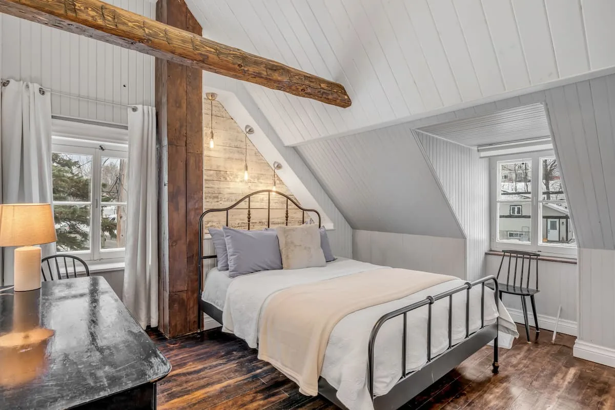 Dormitorio con cama de hierro forjado, viga y pared de piedra