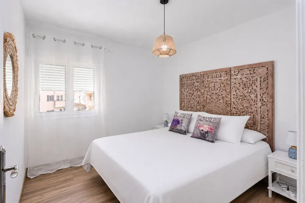 Un dormitorio luminoso cuenta con una cama grande con ropa de cama blanca y un cabecero de madera tallada.