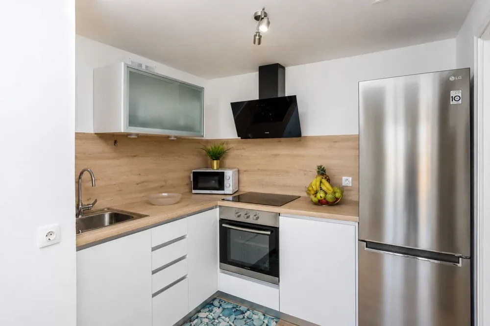 Una cocina moderna con gabinetes blancos, encimeras de madera y electrodomésticos de acero inoxidable.
