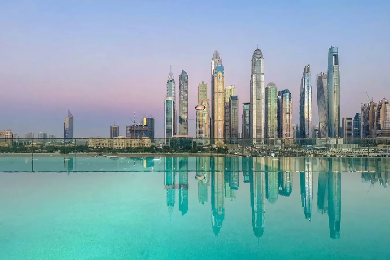 Un horizonte urbano se alza detrás de una piscina turquesa, con los edificios reflejados en el agua.