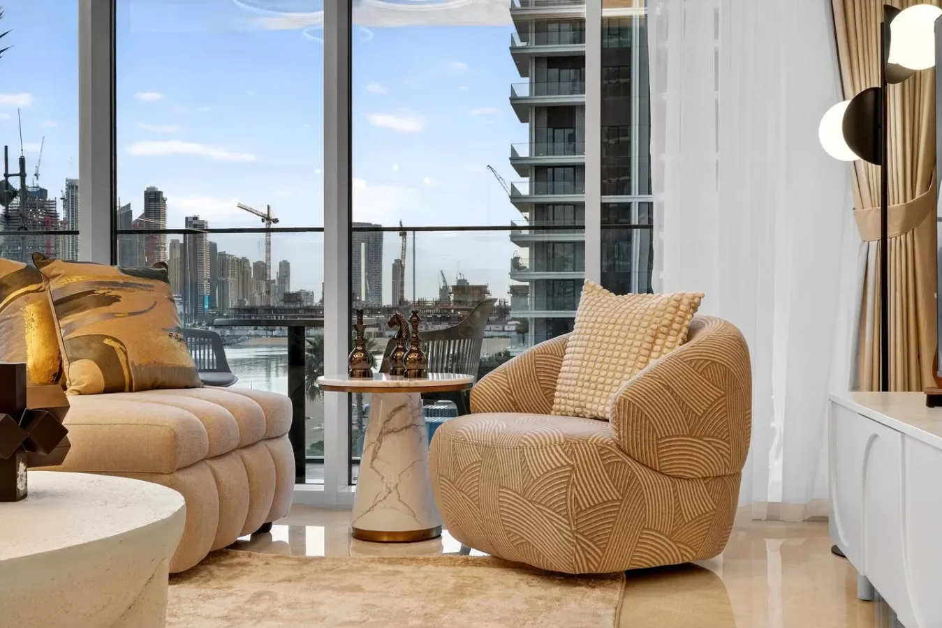 A bright living room with seating beside floor-to-ceiling windows overlooking the city.