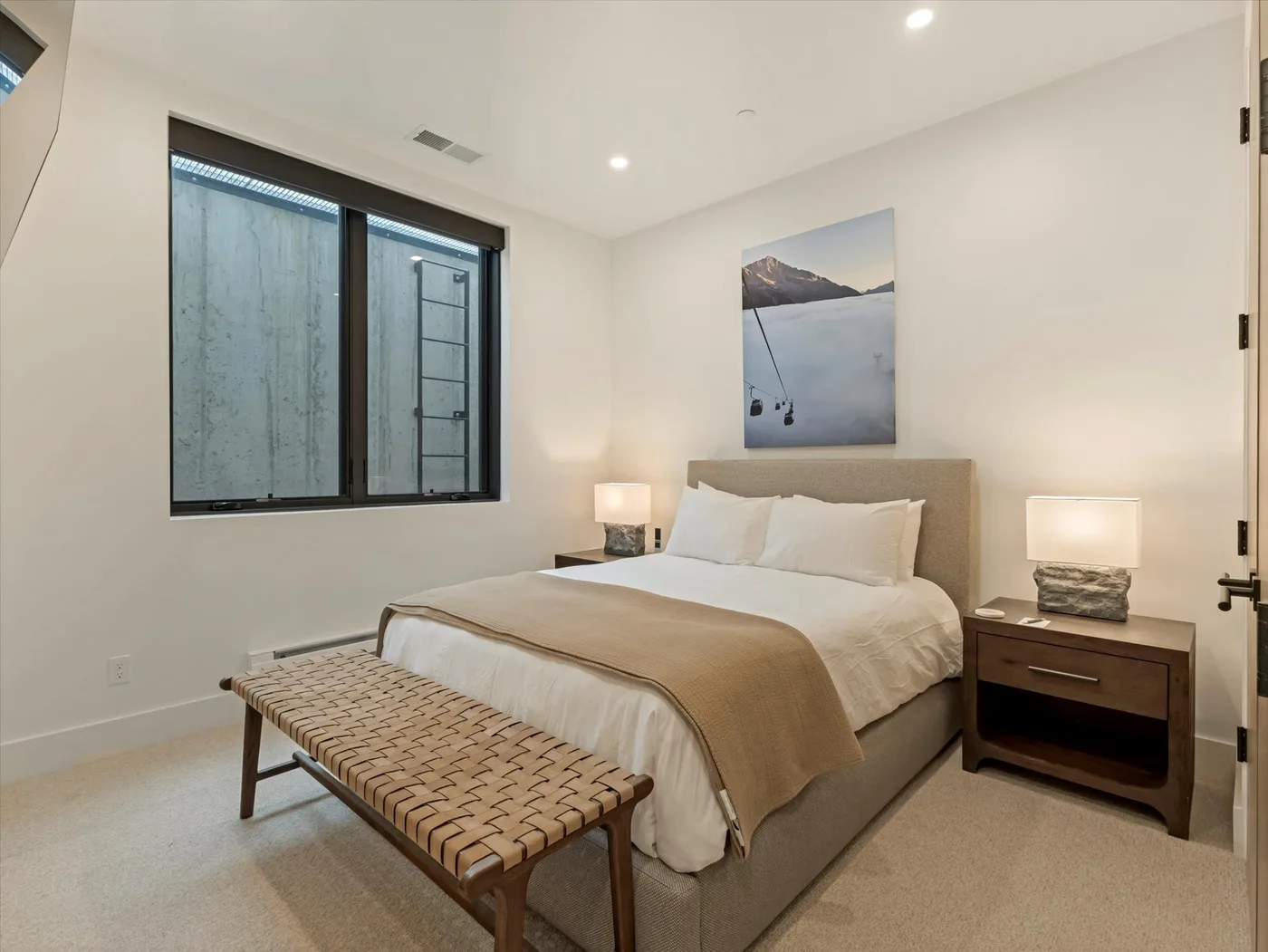 A bedroom with a neatly made bed, bedside tables, and a woven bench.