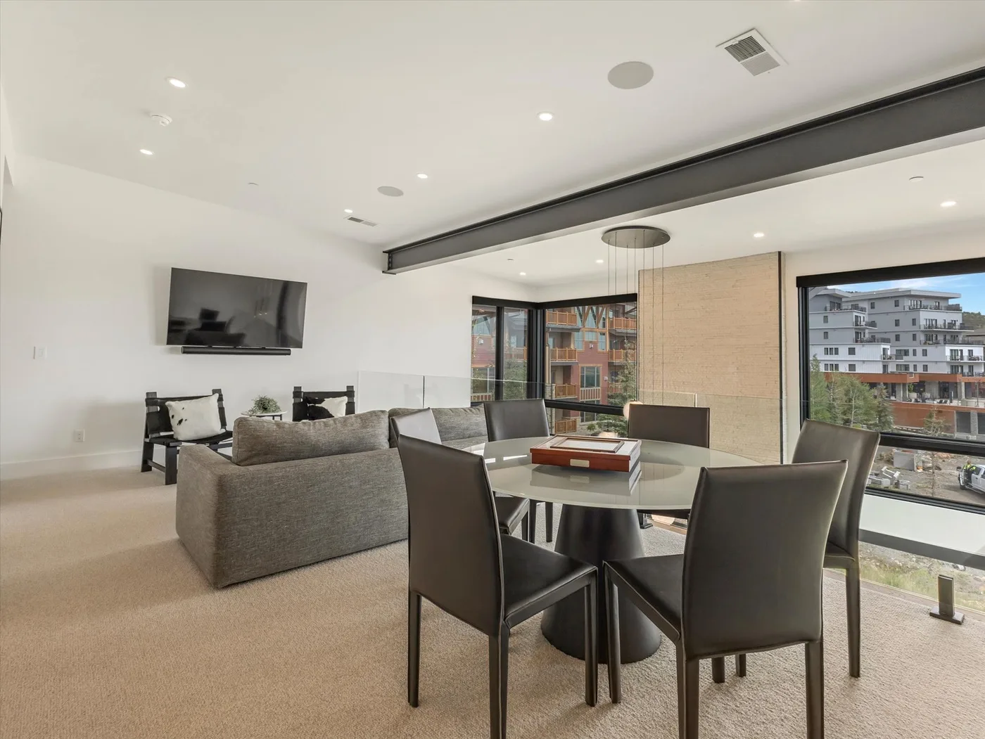 A bright living and dining area with seating, a dining table, and large windows.