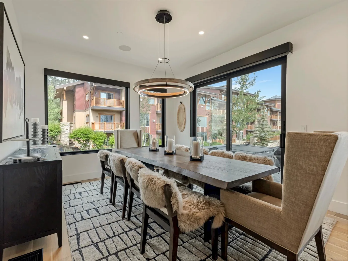 A dining area with a long table and large windows overlooking nearby buildings.