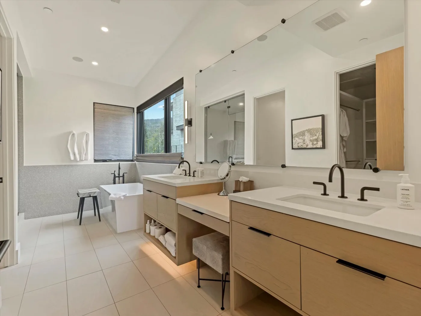 A bright bathroom with long vanity counters, mirrors, and a glass shower.