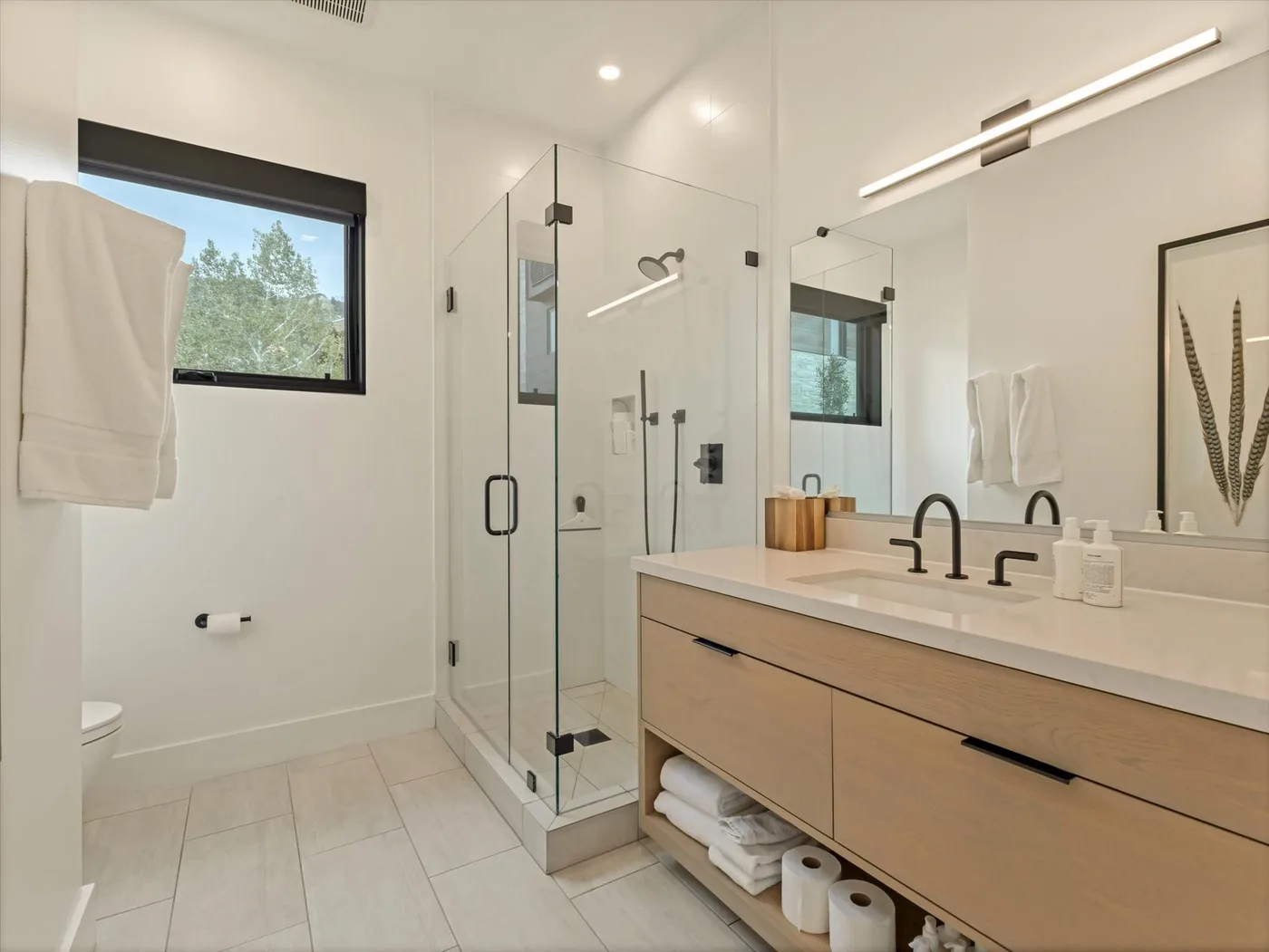 A bright bathroom with a glass shower and a long vanity.