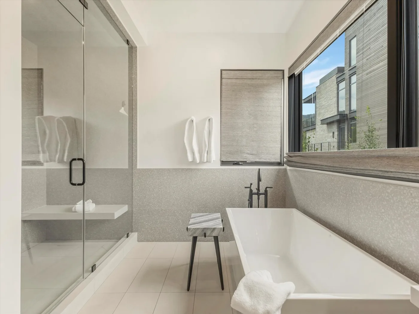 A modern bathroom with a bathtub, glass shower, and a large window.