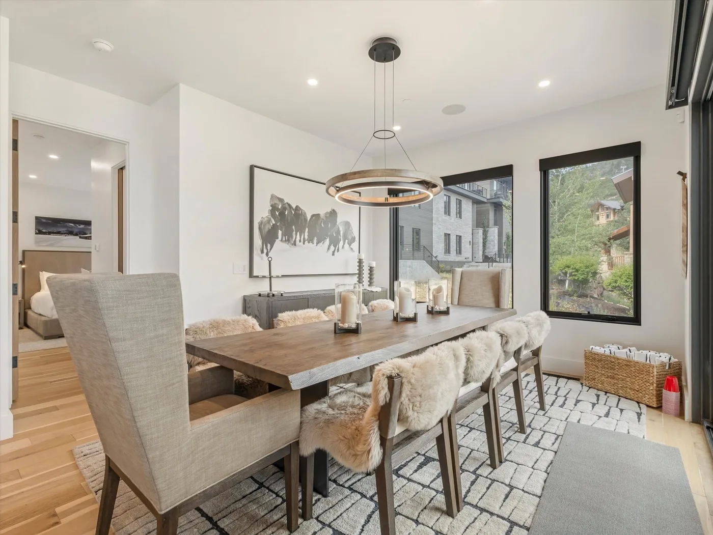 A dining area with a long wooden table, upholstered seating, and large windows.