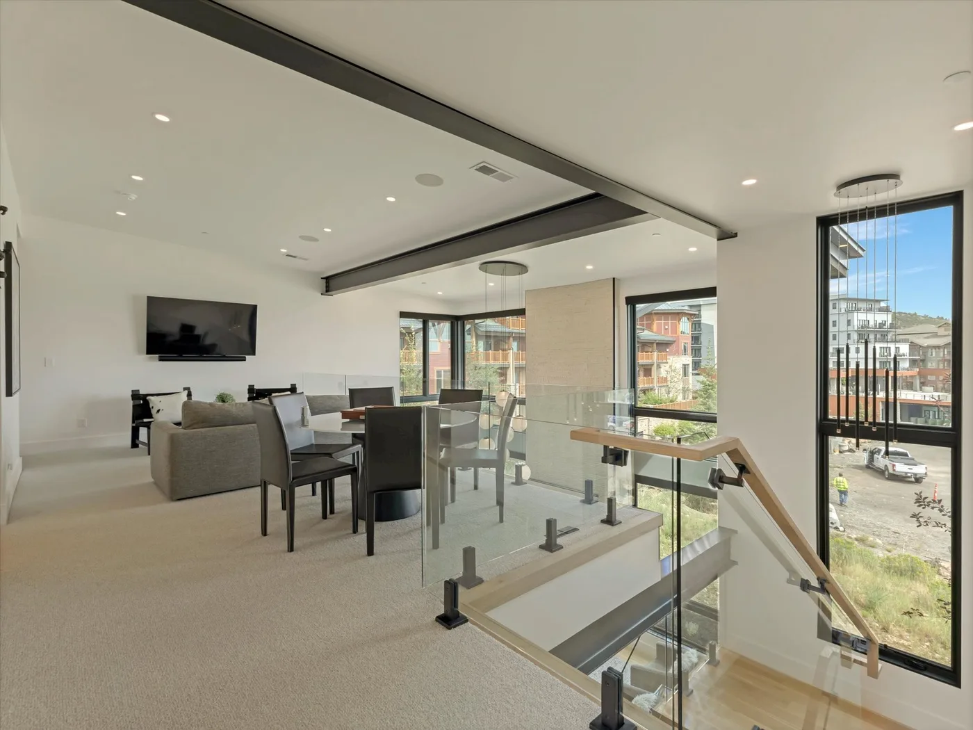 A bright open-plan living and dining area with large windows and a glass stair railing.