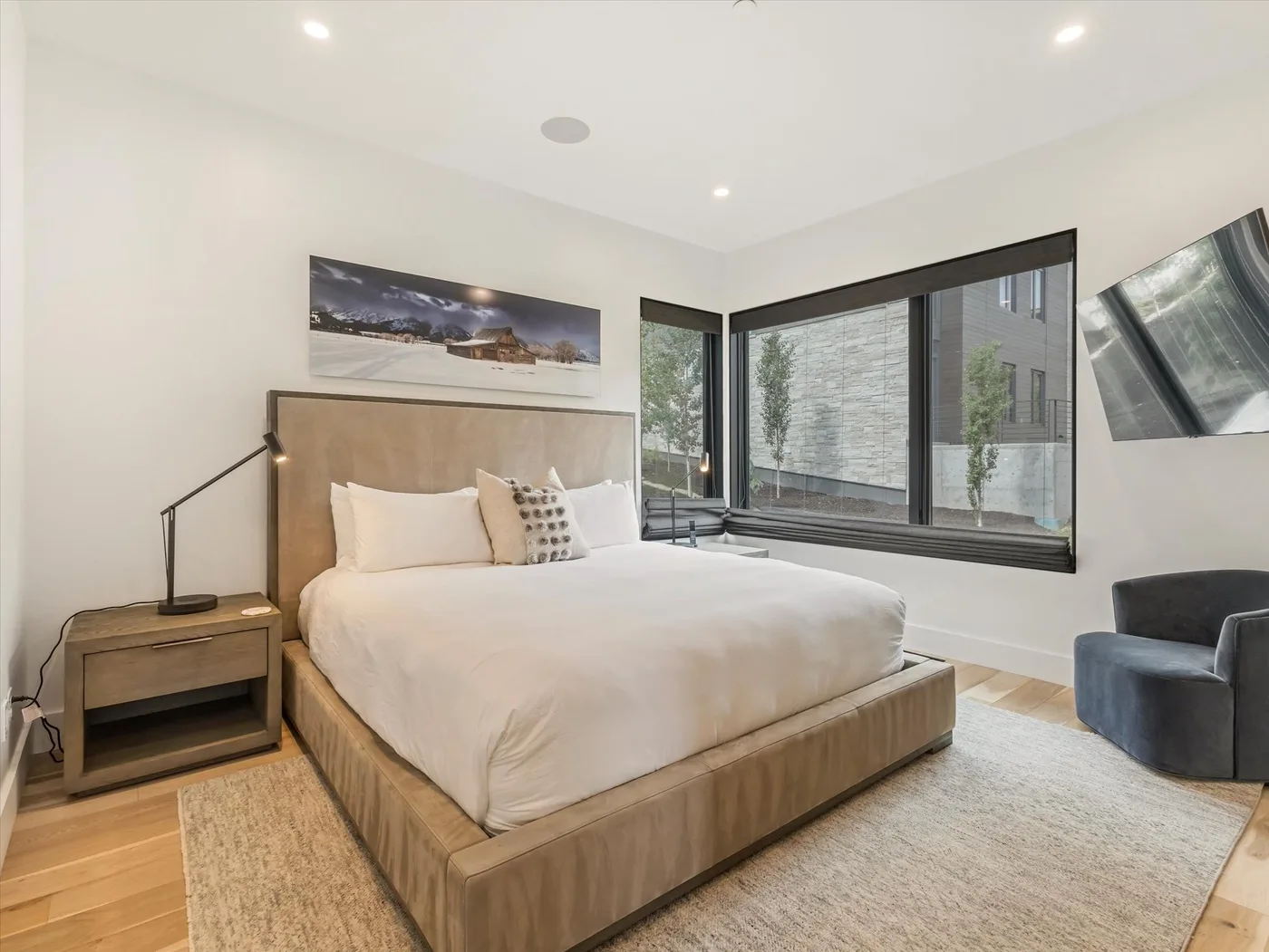 A bedroom with a large bed, bedside table, and broad windows.