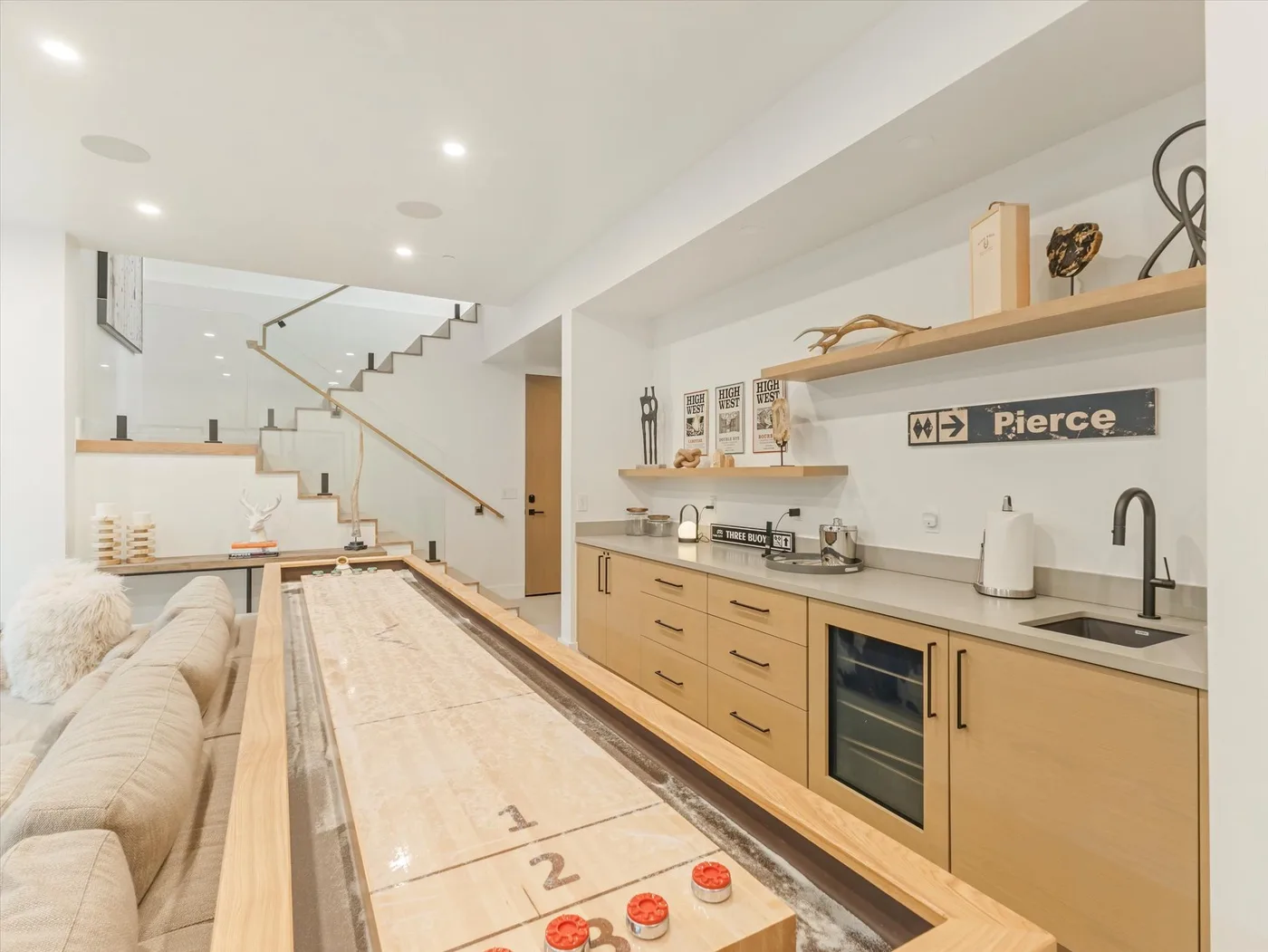 A bright open-plan room with a long shuffleboard table and a kitchen counter.