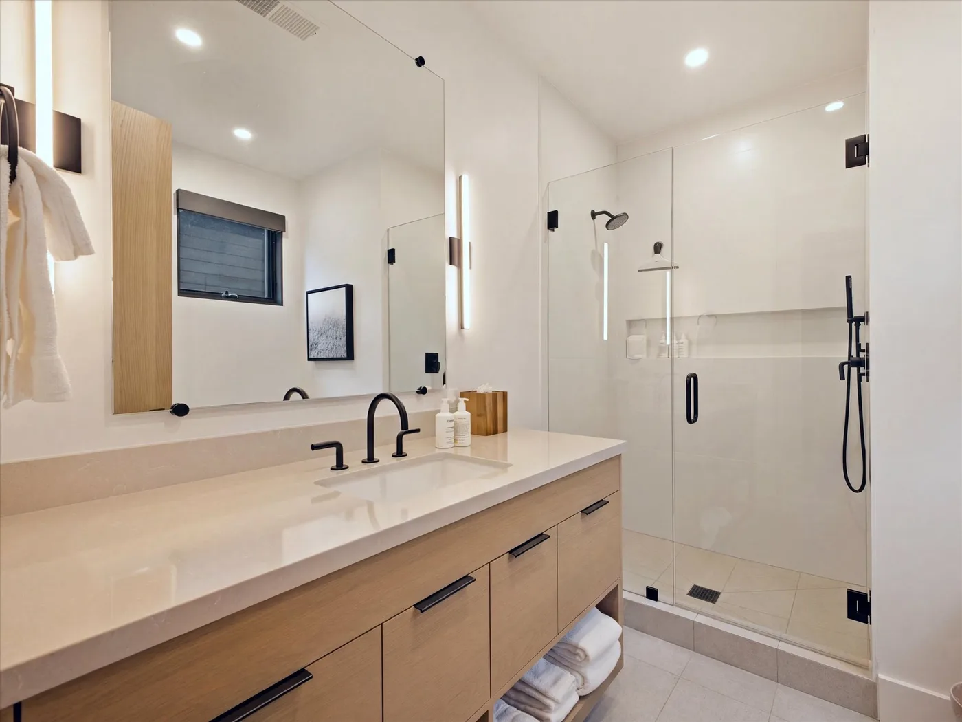 A bright bathroom with a long vanity and glass shower.