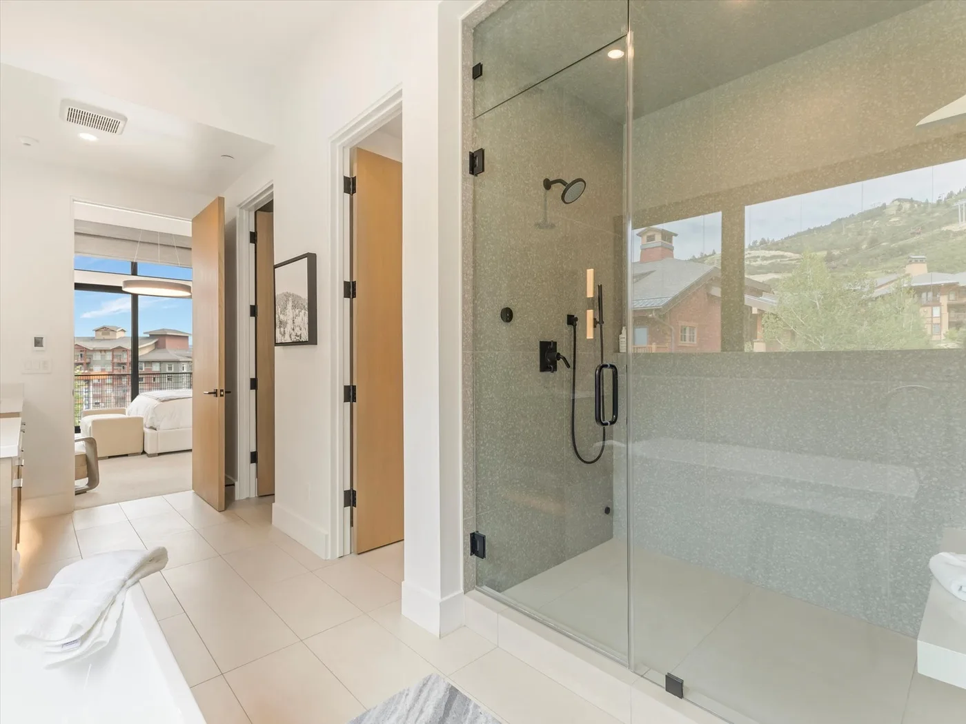A bathroom with a glass shower and an open view into an adjoining room.