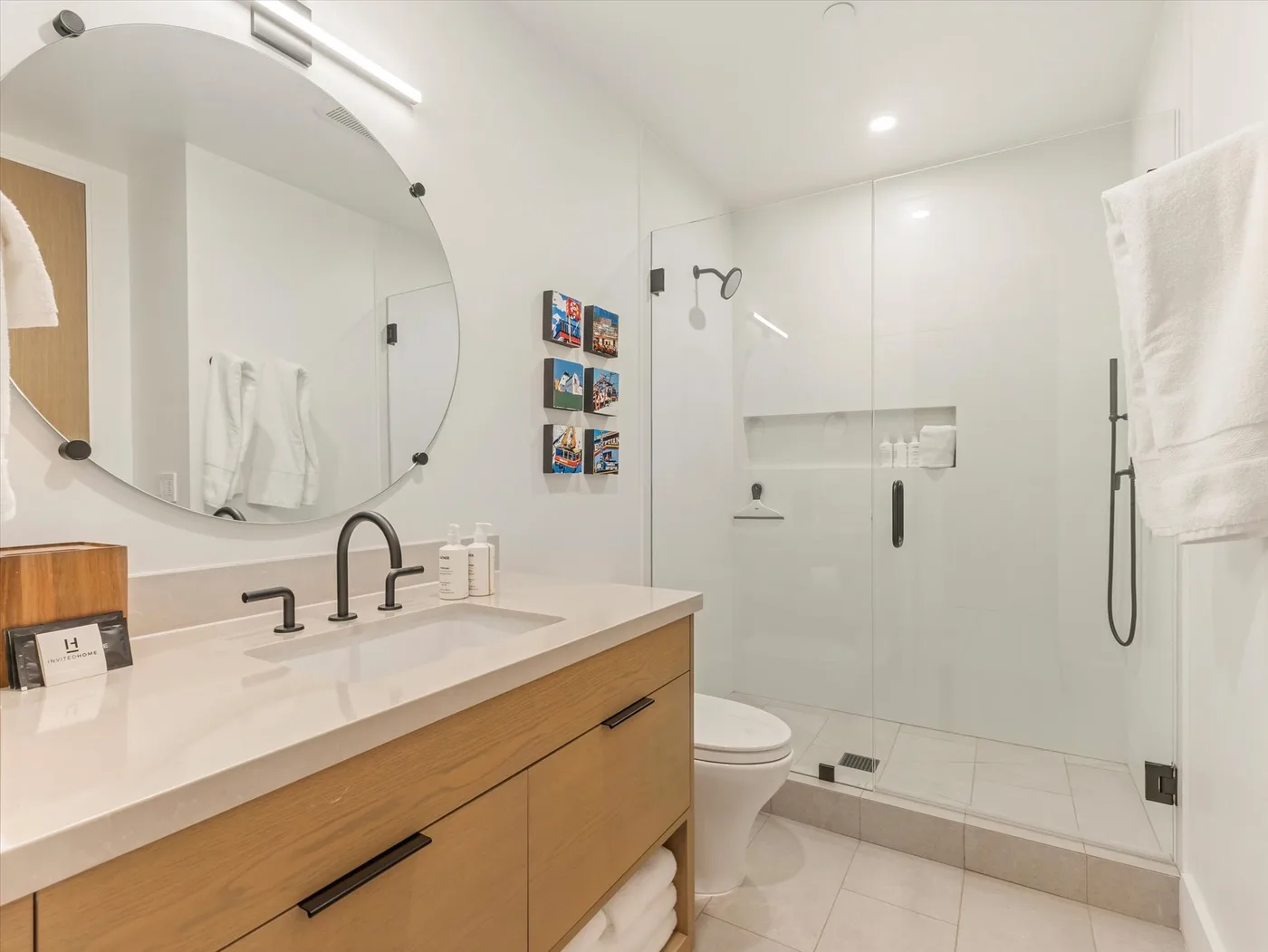 A bright bathroom with a long vanity, round mirror, and walk-in shower.