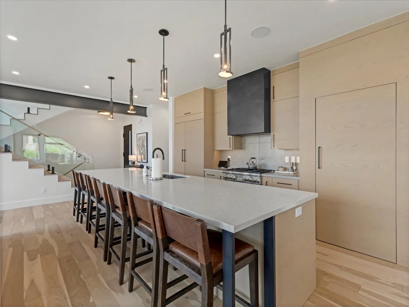 A modern kitchen with a long island and seating beneath pendant lights.