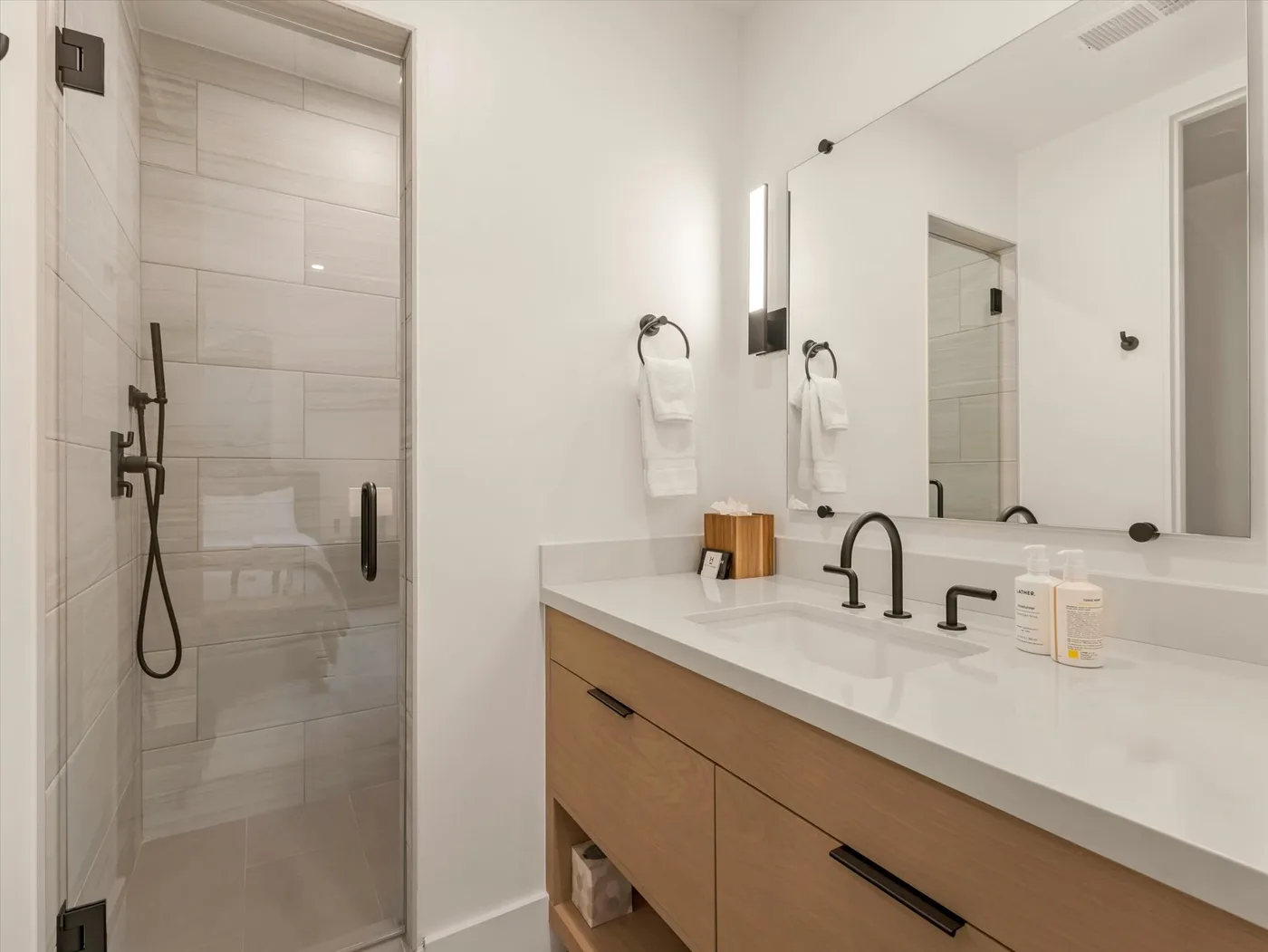 A bathroom with a glass shower and a long vanity beneath a large mirror.
