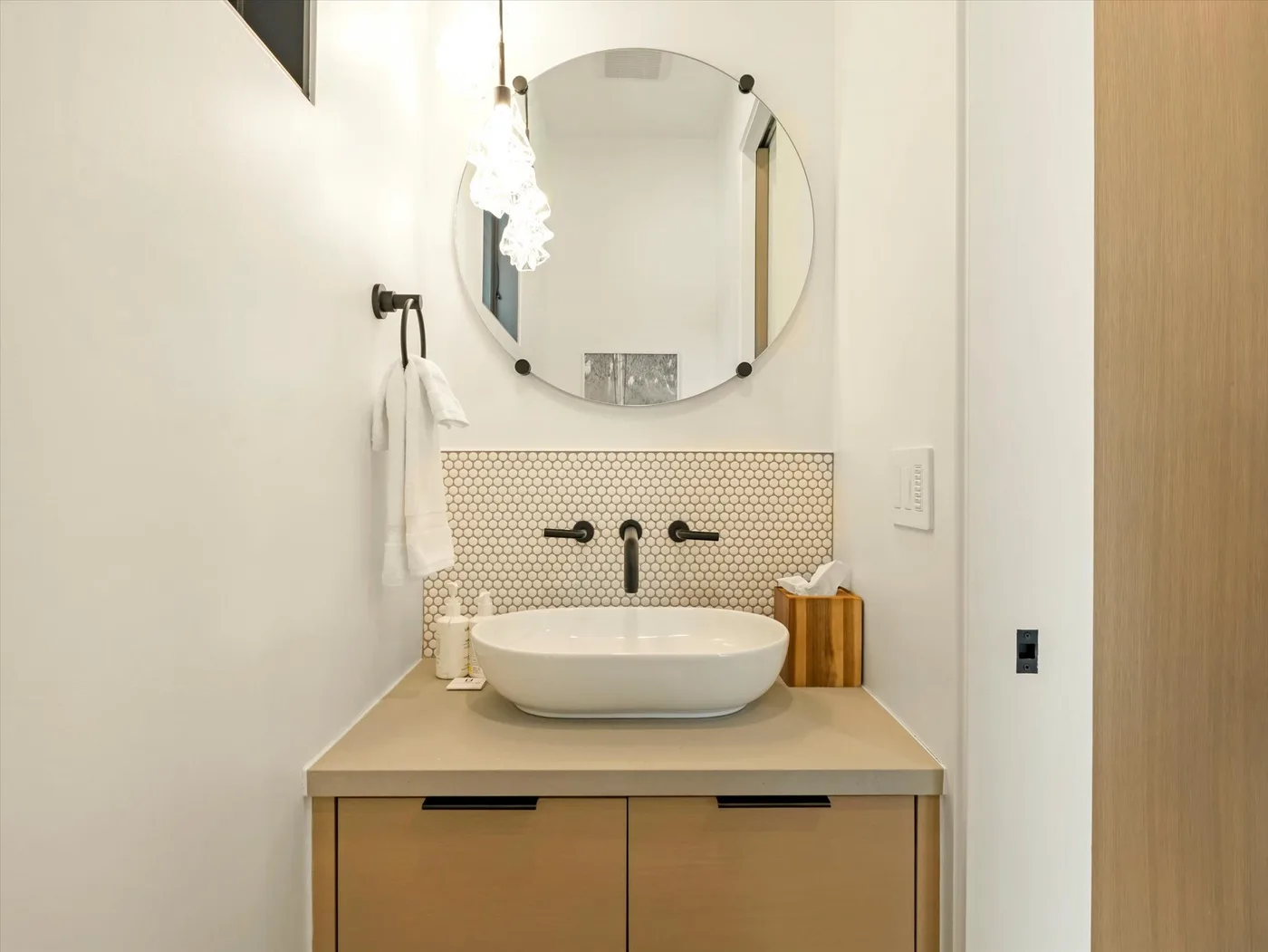 A bathroom vanity with a vessel sink, wall-mounted faucet, and round mirror.