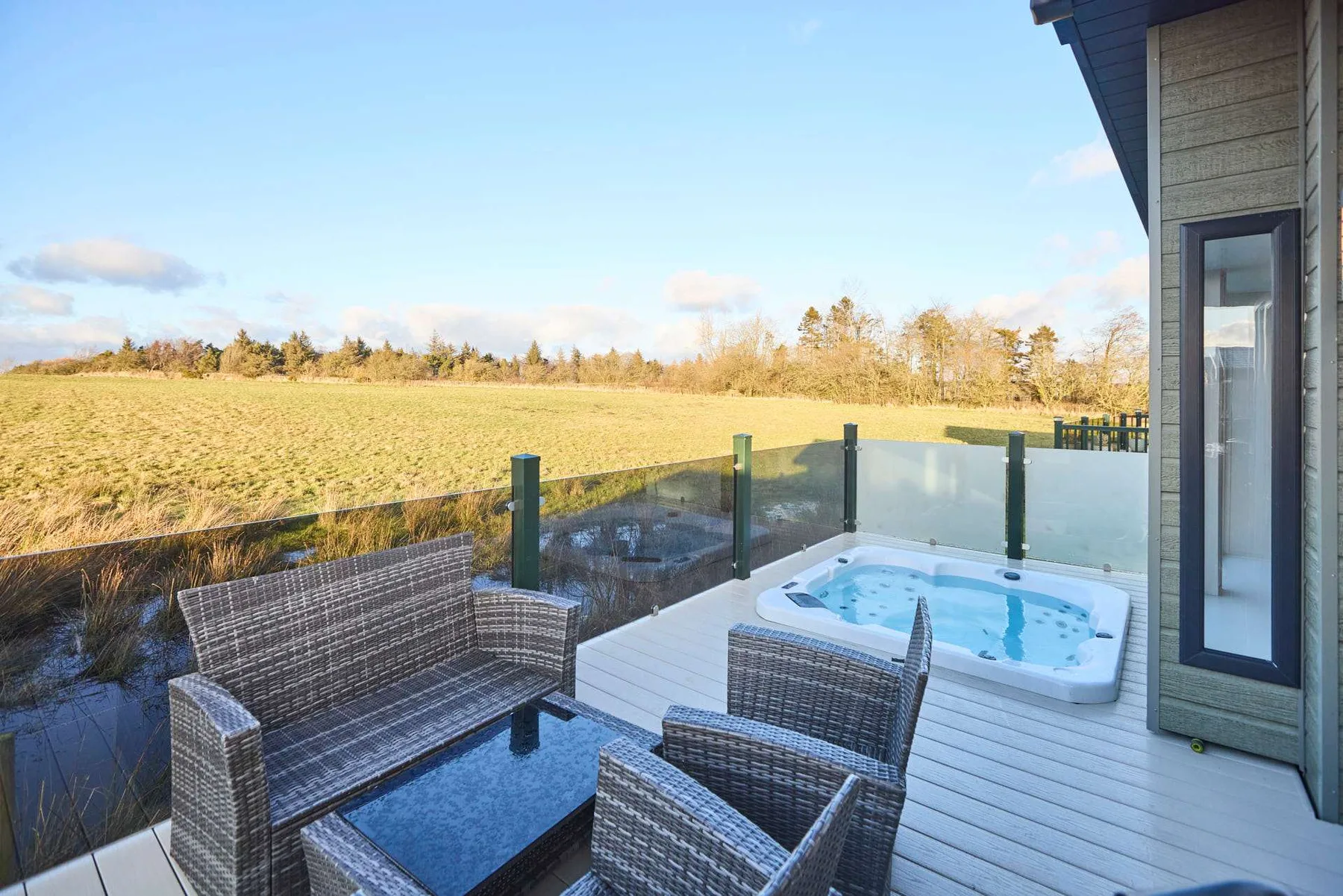 Una terraza con jacuzzi y asientos al aire libre da a un campo abierto.