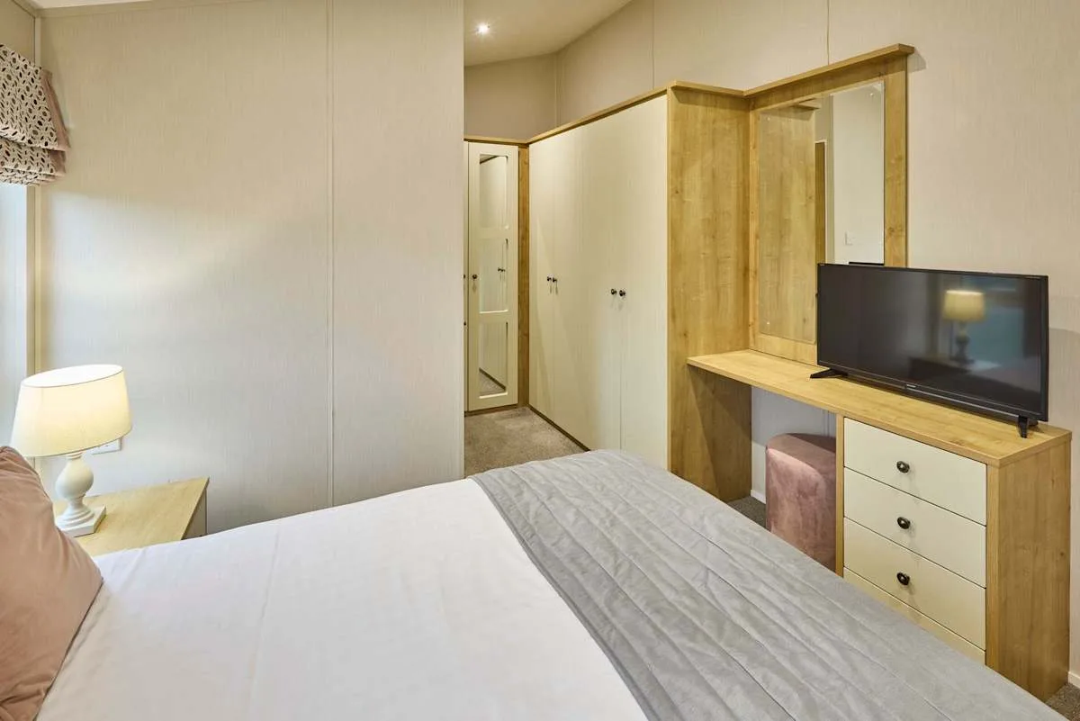 Un dormitorio con cama, lámpara de noche y escritorio de madera con televisor.