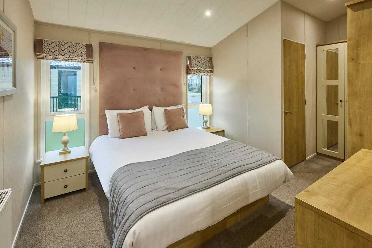 Un dormitorio con una cama entre dos ventanas y mesas de noche.
