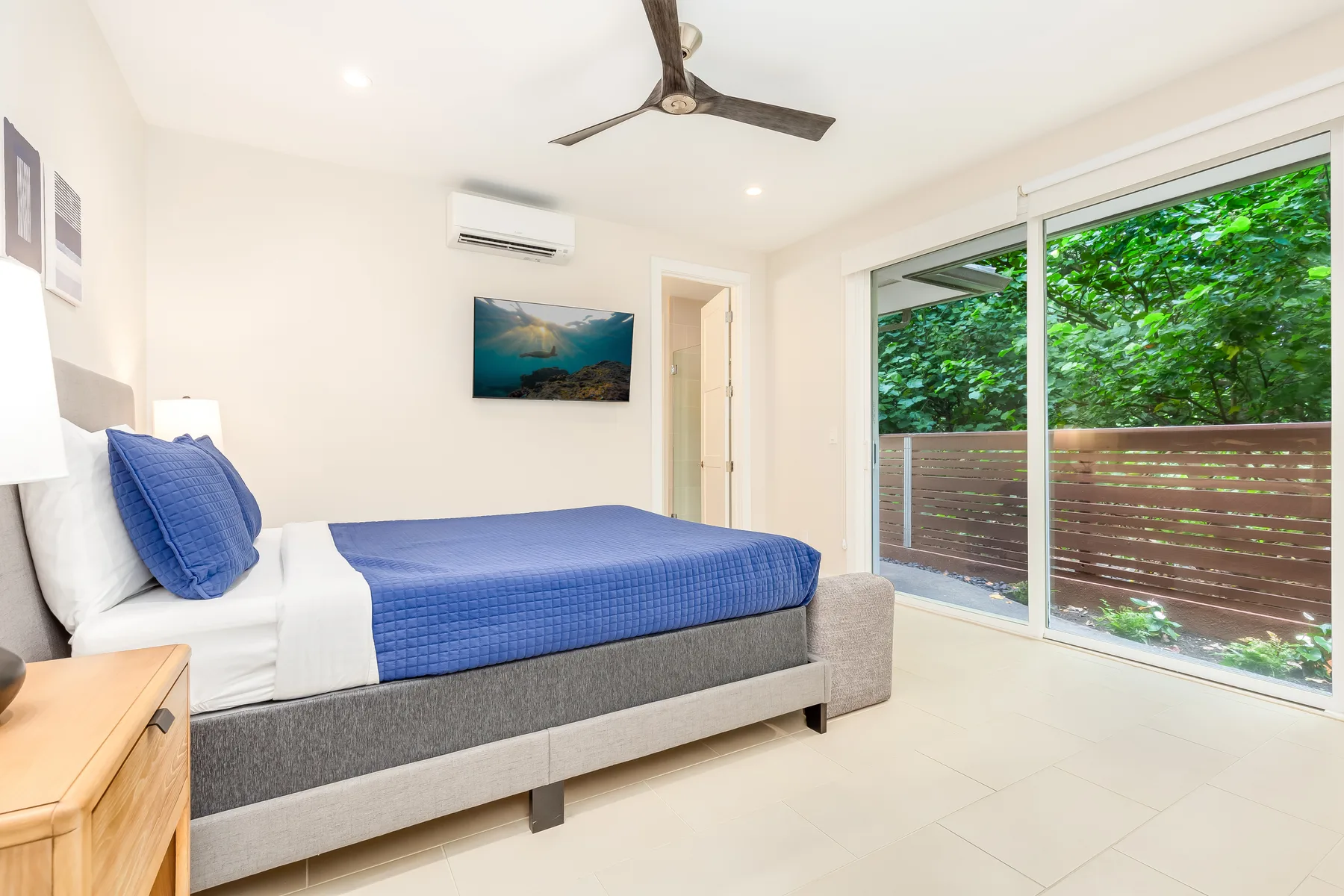 Un dormitorio con una cama junto a puertas corredizas de vidrio y una vista frondosa.