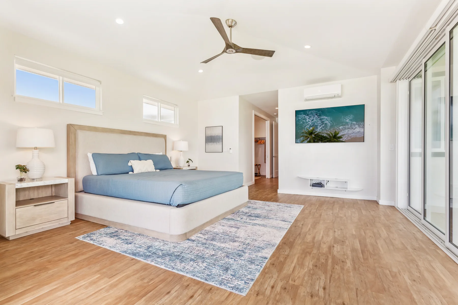 Un dormitorio luminoso con una cama azul, un ventilador de techo y puertas corredizas de vidrio.