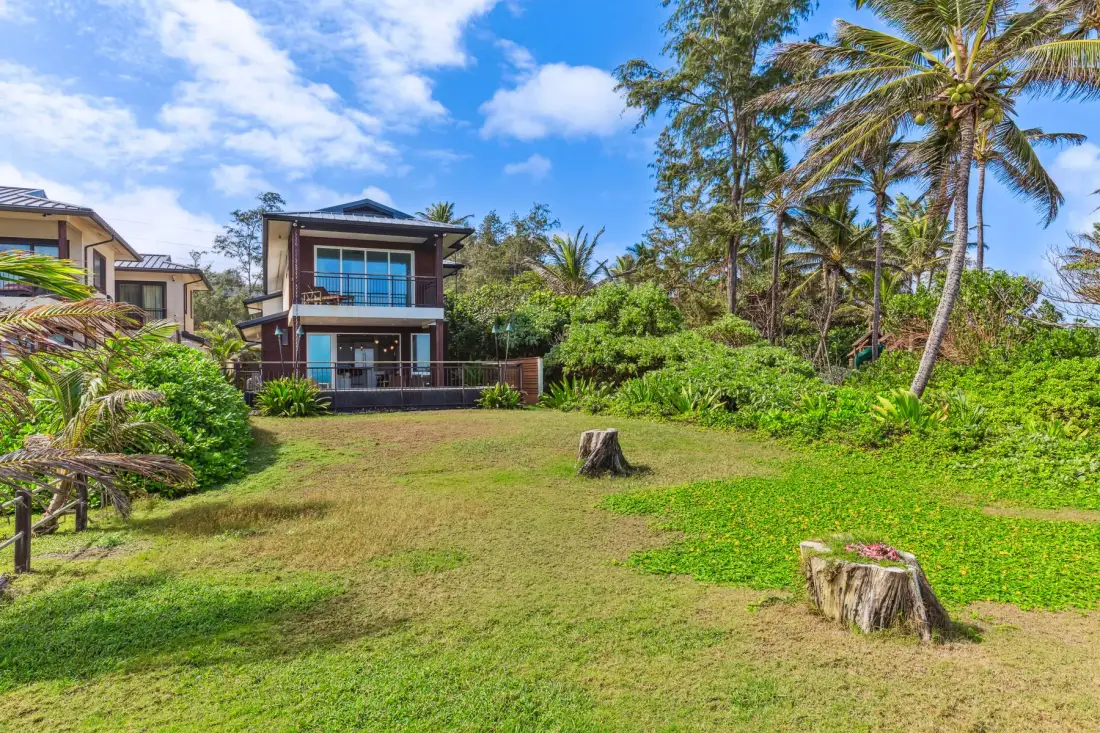 Un césped ajardinado con una casa moderna y palmeras tropicales.