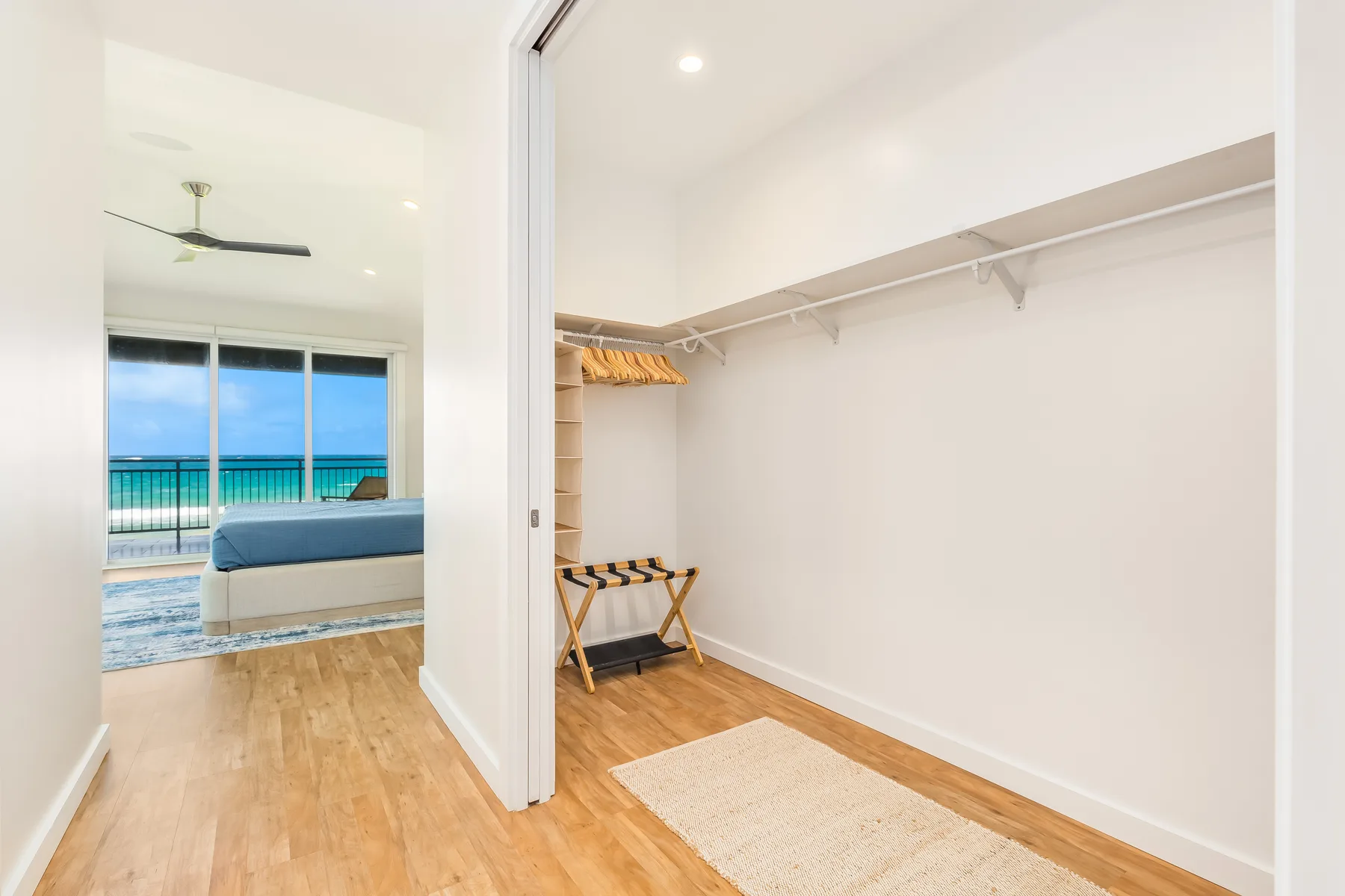 Un armario abierto con espacio para colgar junto a un dormitorio con vista al mar.
