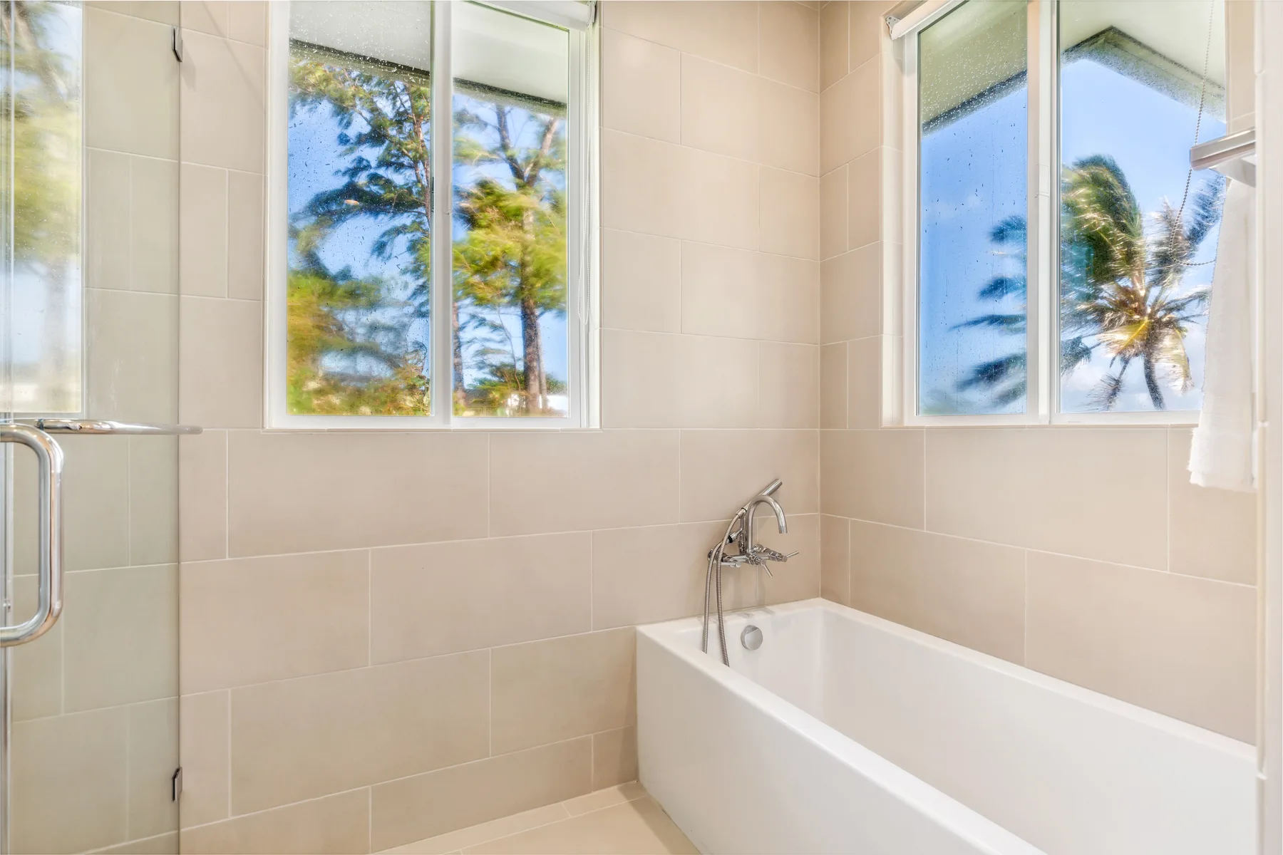Un baño alicatado con una bañera bajo ventanas luminosas.
