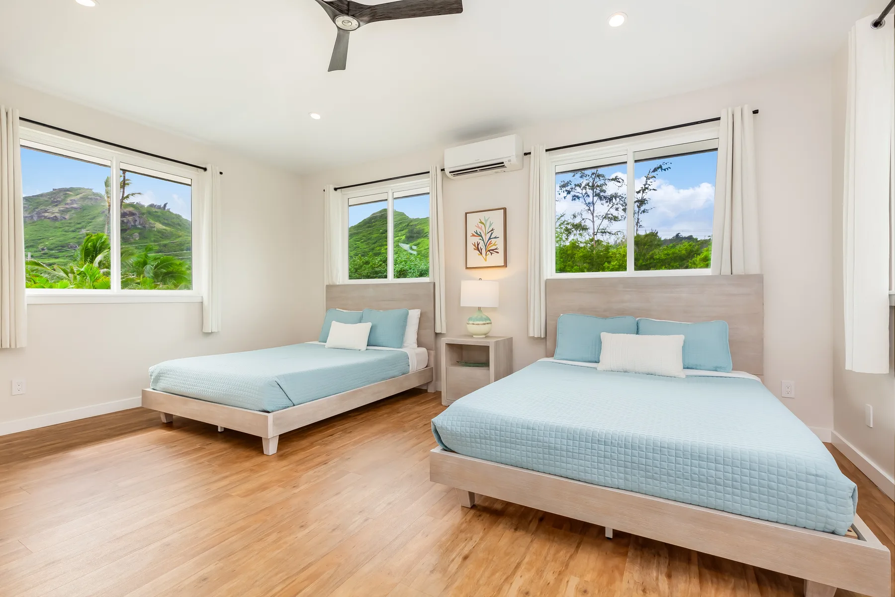 Un dormitorio luminoso con dos camas y ventanas con vistas a colinas verdes.