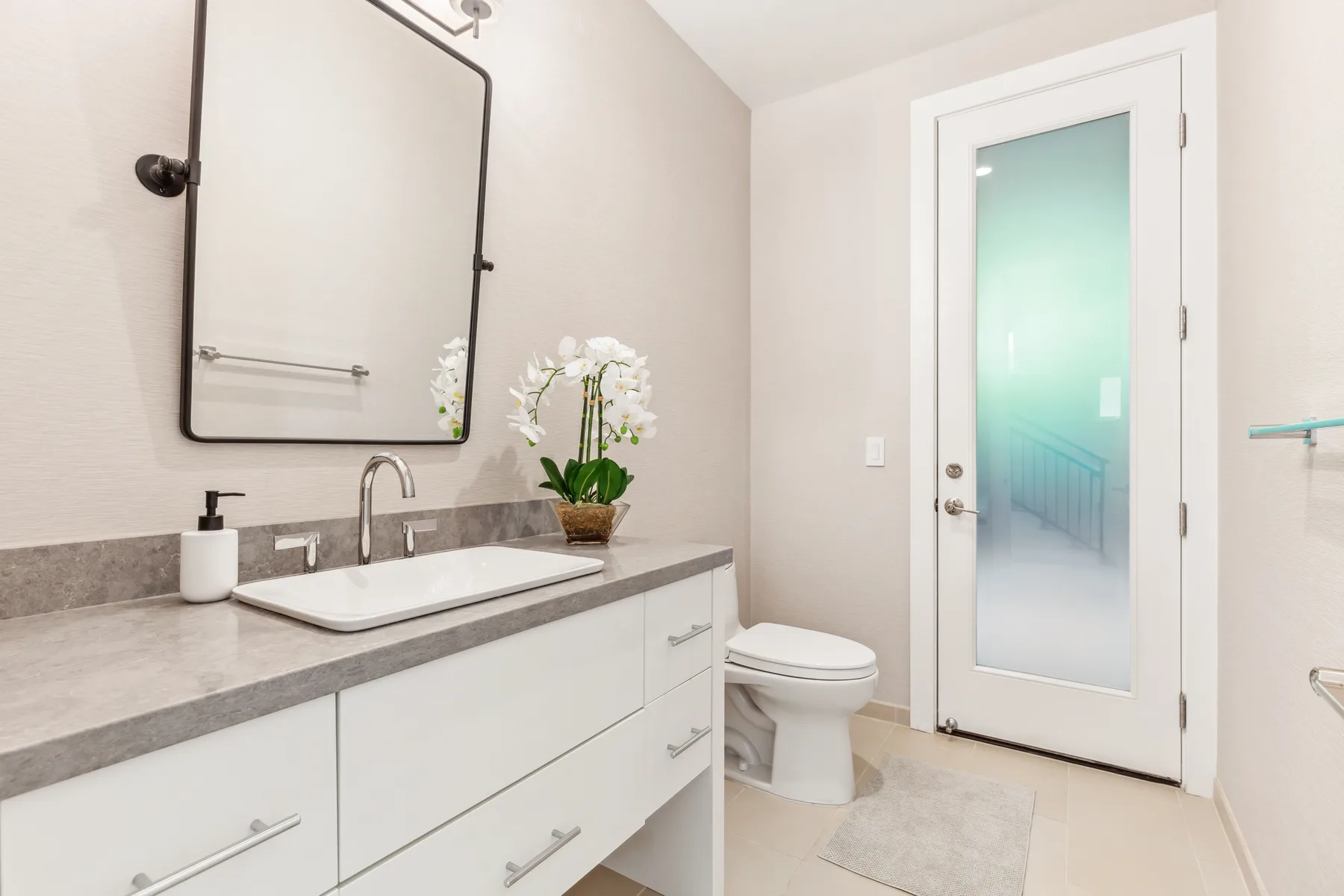 Un baño con tocador, lavabo, espejo y puerta de vidrio esmerilado.