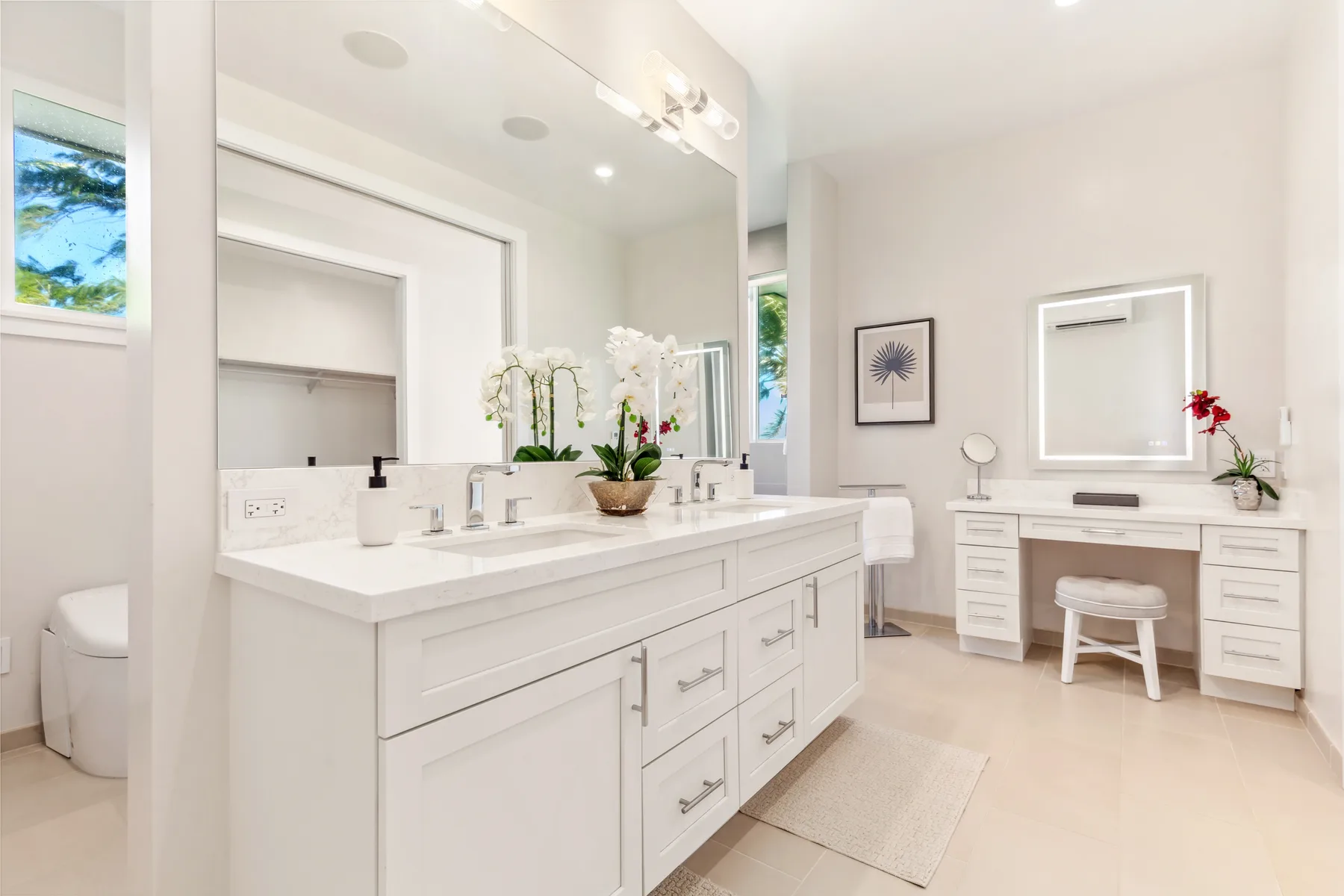 Un baño luminoso con un largo tocador, lavabos y una mesa de maquillaje aparte.