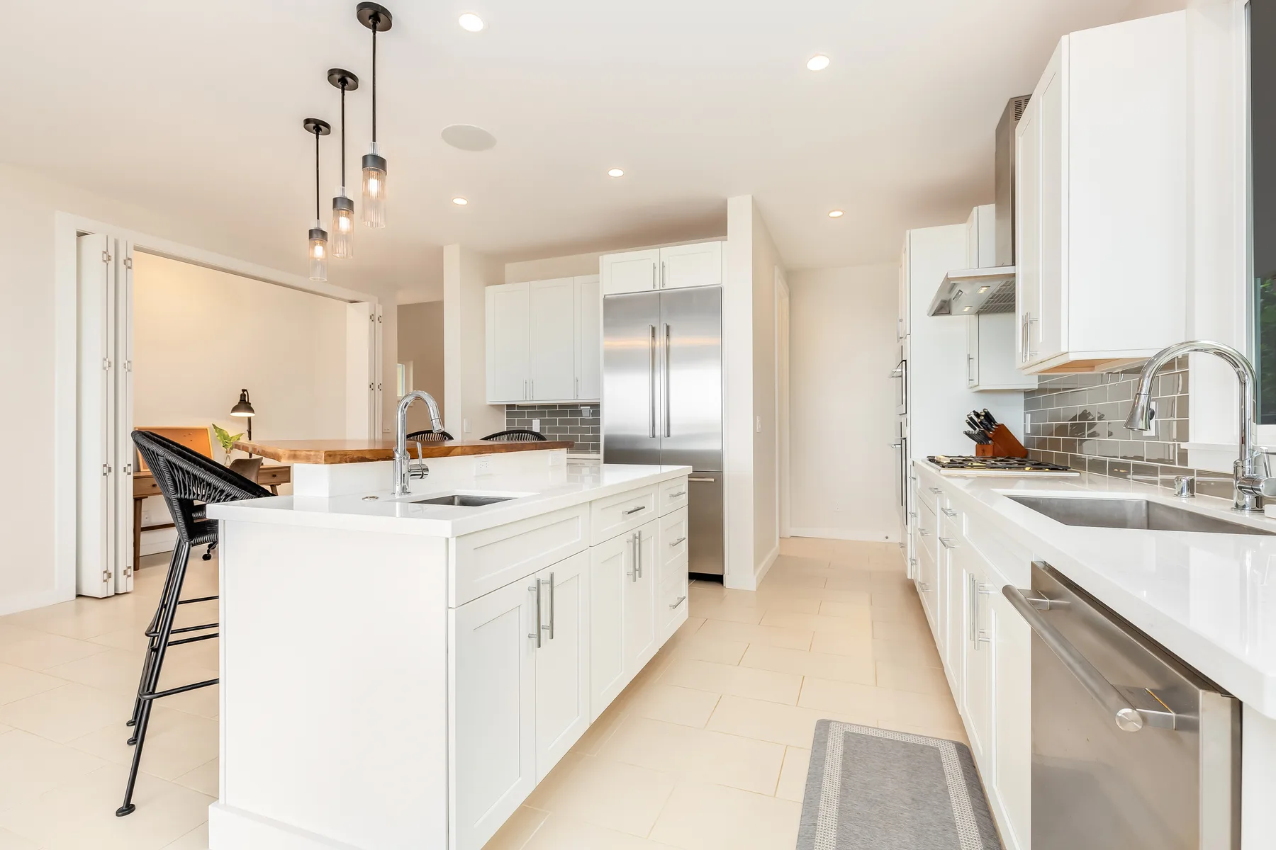 Una cocina luminosa con una isla central, gabinetes blancos y electrodomésticos de acero inoxidable.