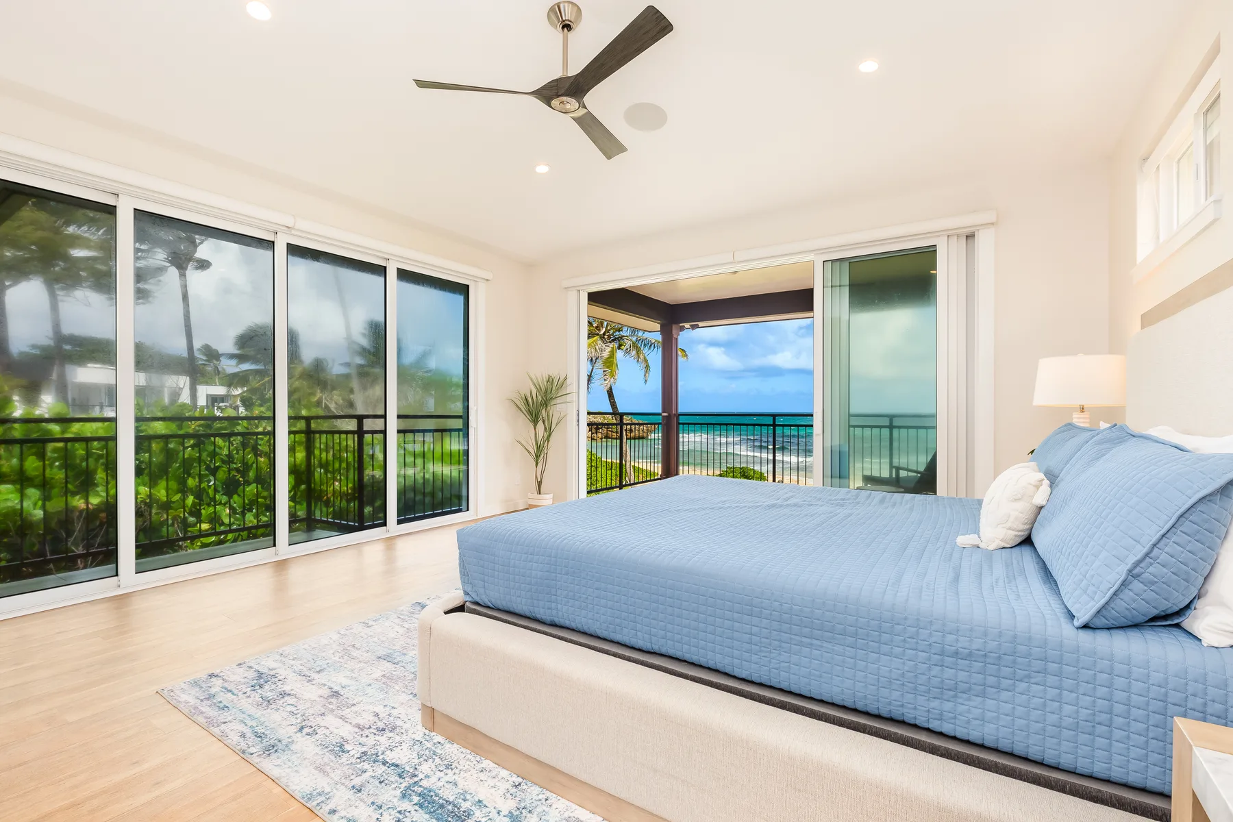 Un dormitorio luminoso con una cama azul junto a grandes ventanas con vistas al océano.