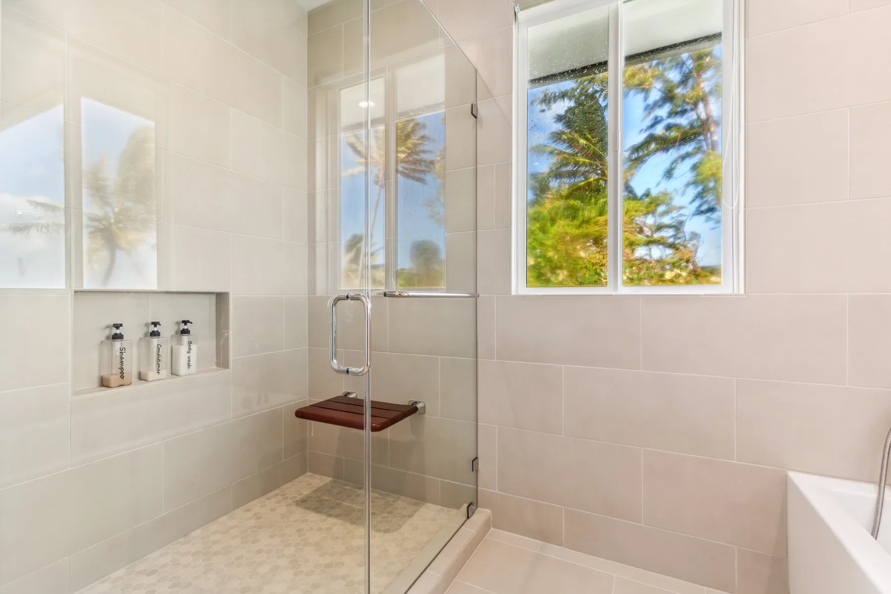 Un baño luminoso con azulejos, una ducha de vidrio y una ventana grande.