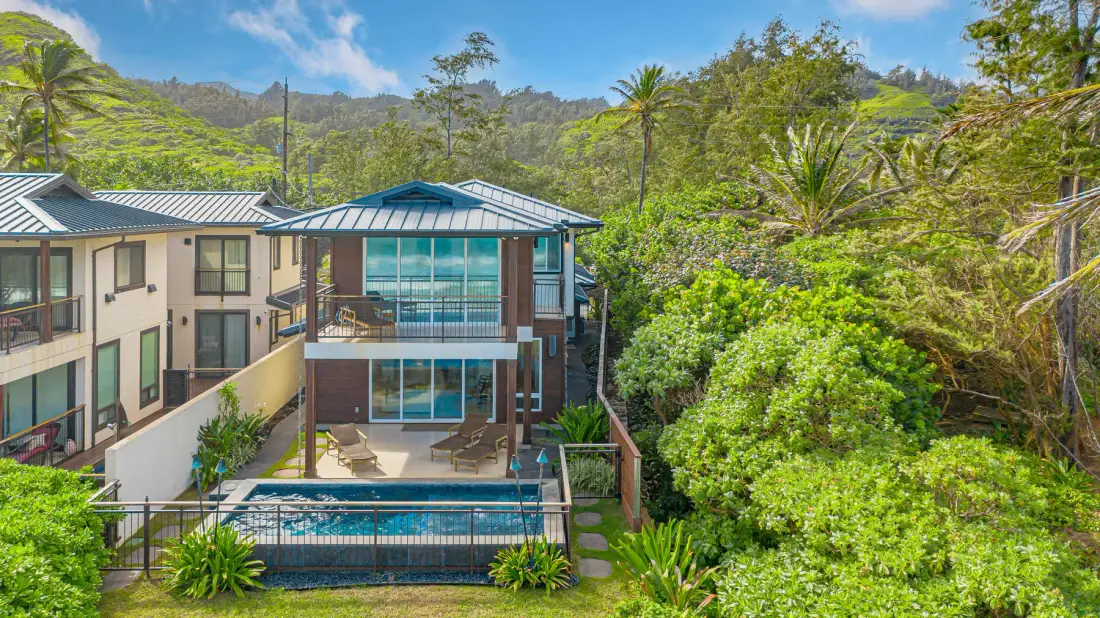 Un edificio moderno y una piscina exterior están rodeados de exuberante vegetación tropical.