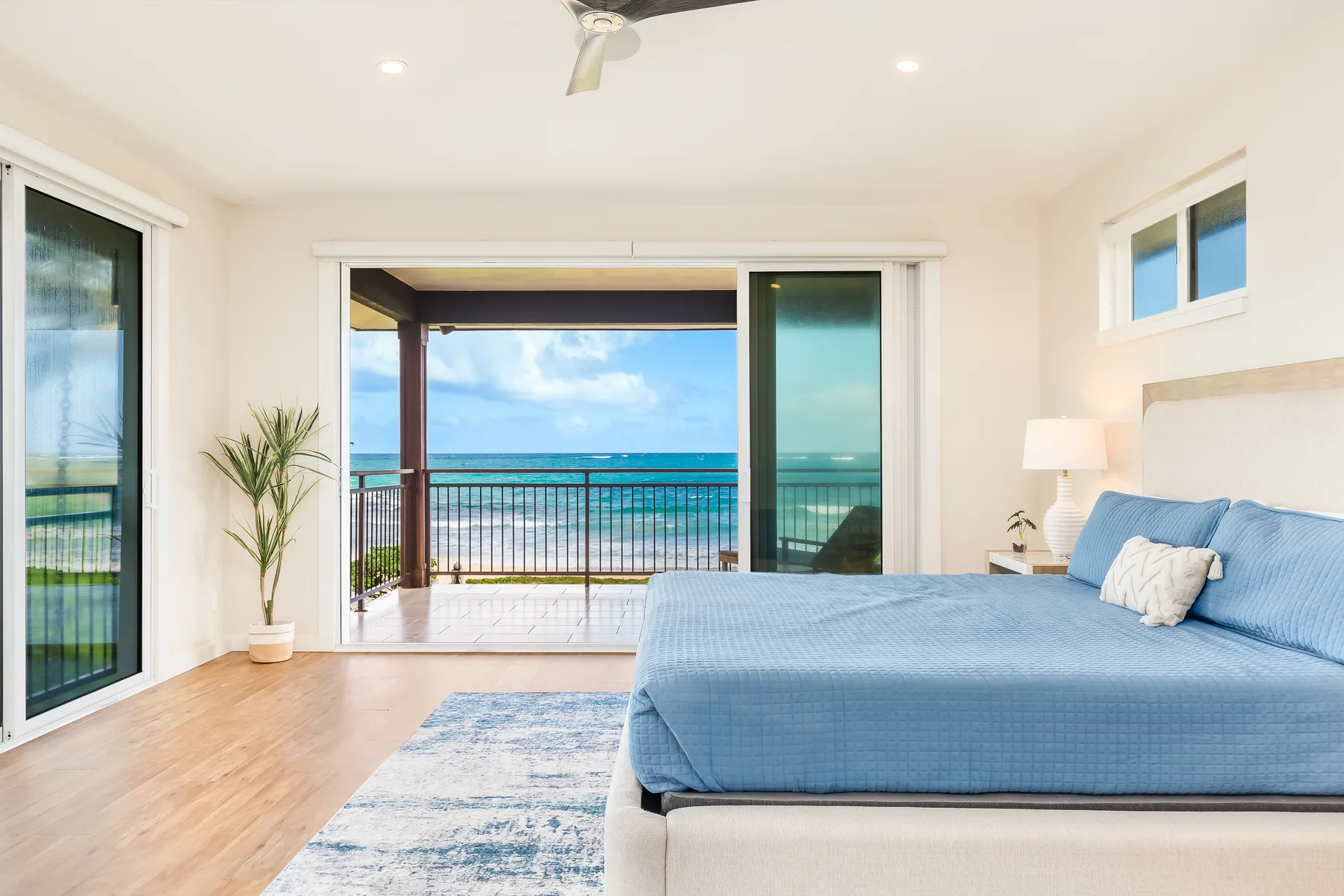 Dormitorio con una cama azul frente a un balcón abierto y vistas al mar.