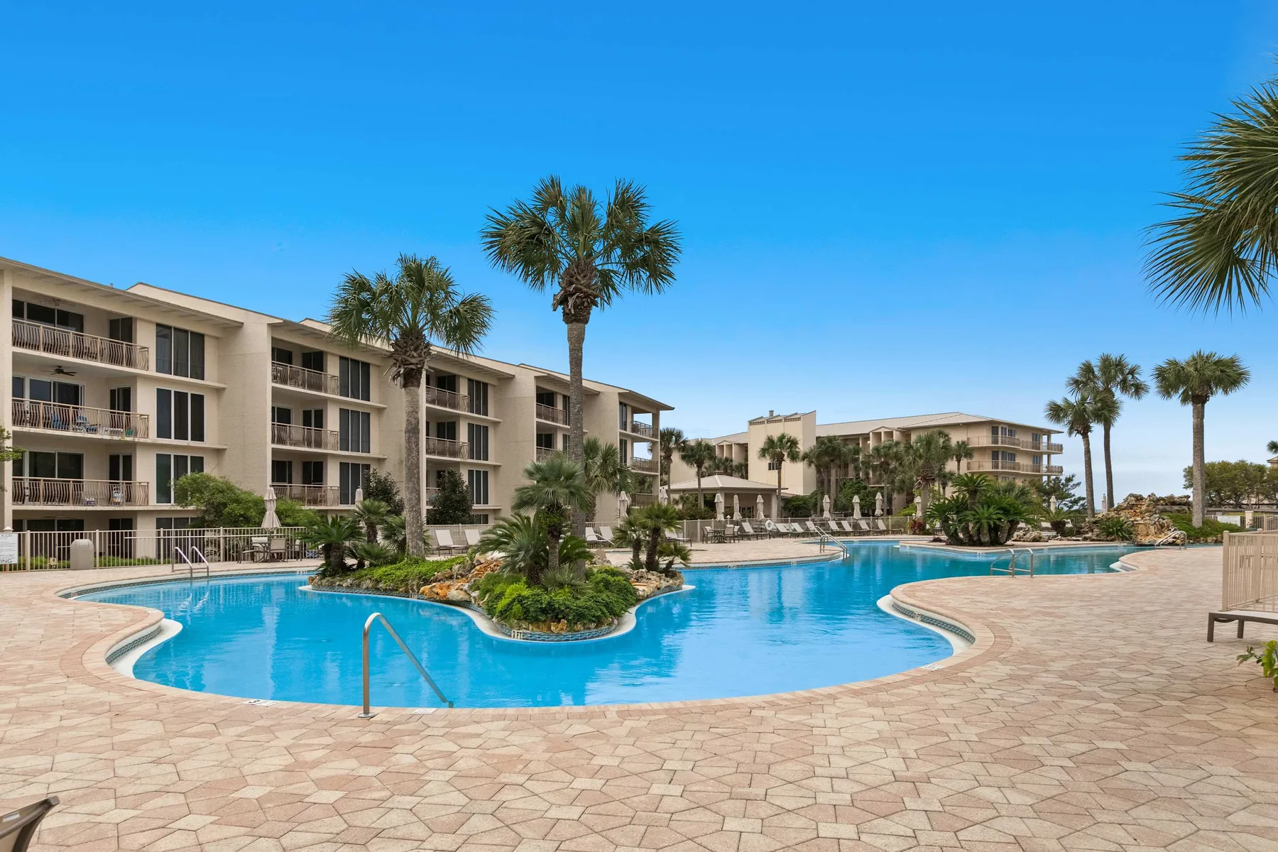 An outdoor swimming pool sits among low-rise buildings and palm trees.