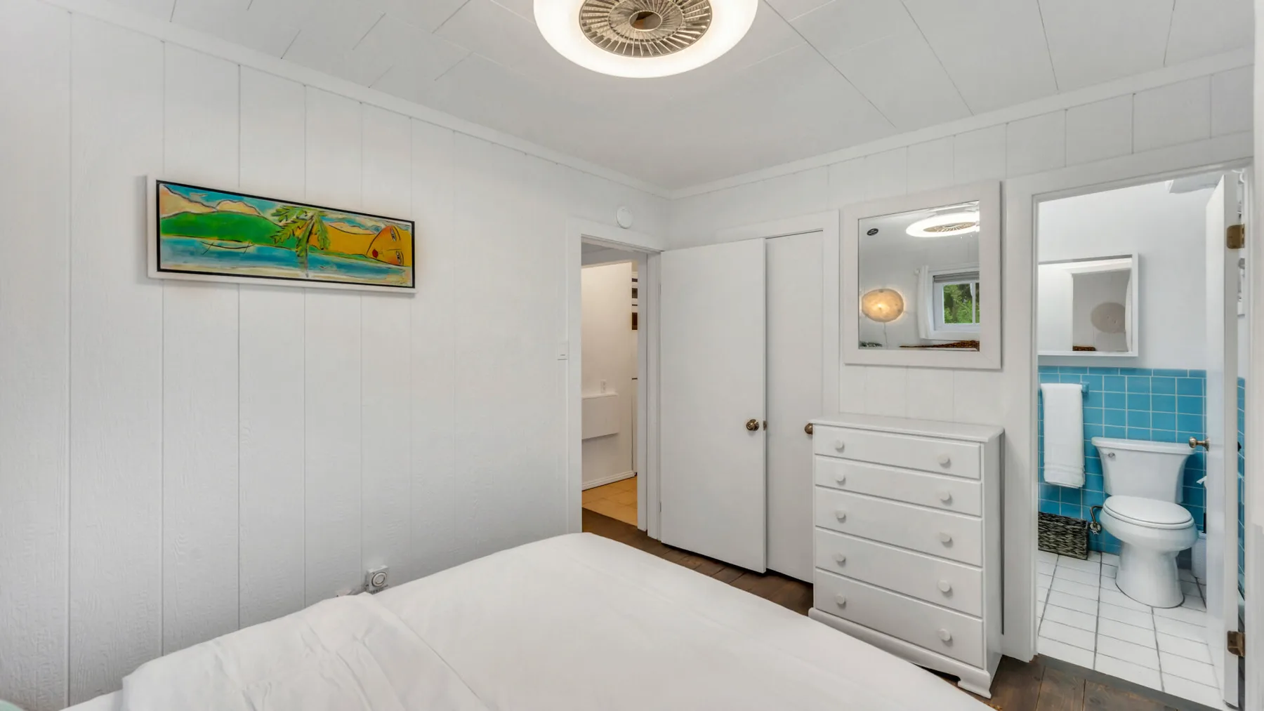 A bright bedroom with a bed, dresser, and open doorway to a bathroom.