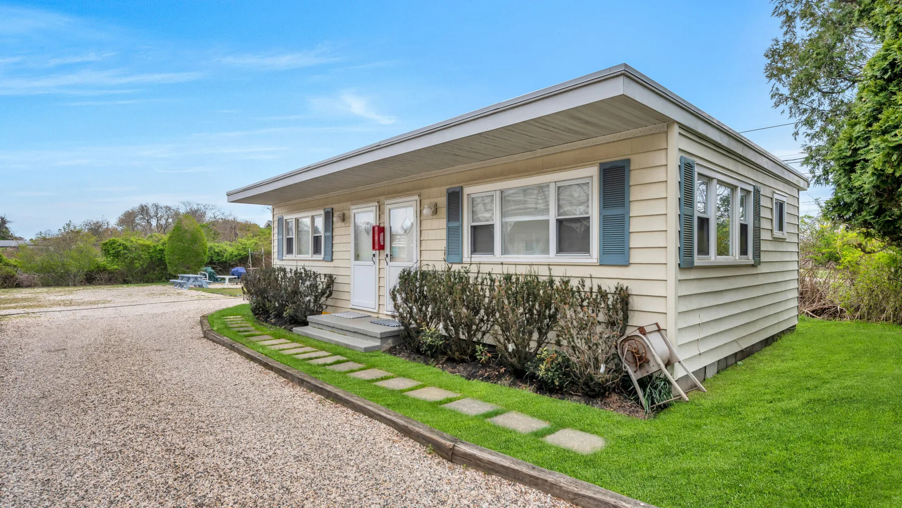 A single-story house stands beside a gravel driveway and a strip of lawn.